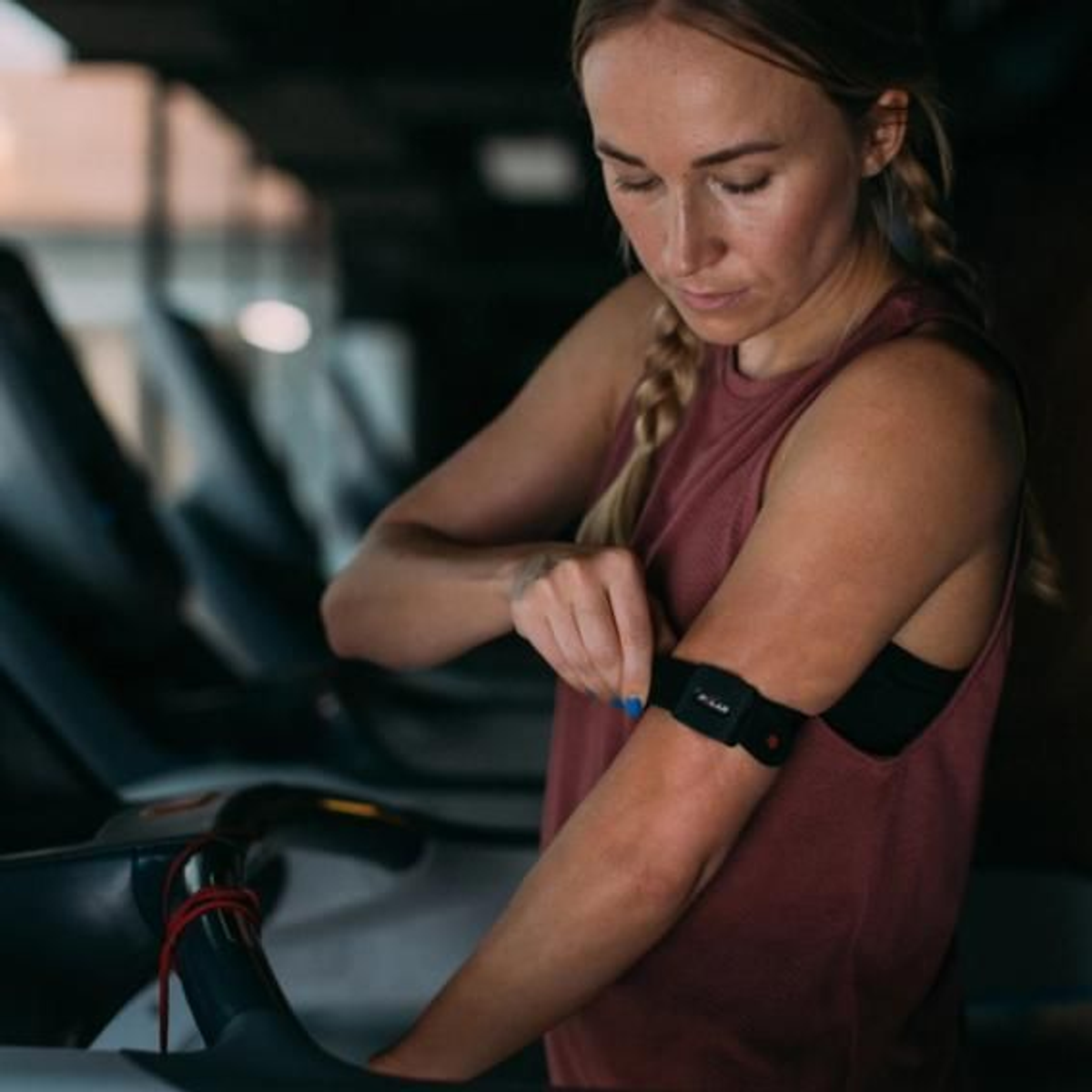 Frau trägt einen Herzfrequenzmesser am Arm, während sie im Fitnessstudio auf dem Laufband steht.