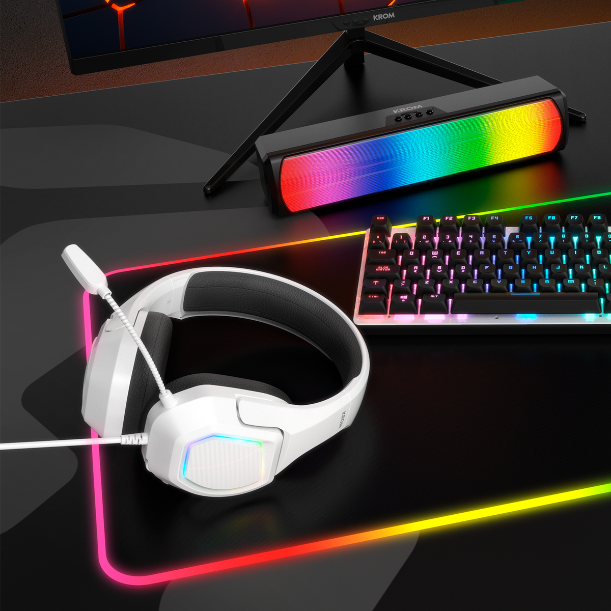Gaming-Setup: Kopfhörer, Tastatur und ein regenbogenfarbener Lautsprecher auf einem Schreibtisch.