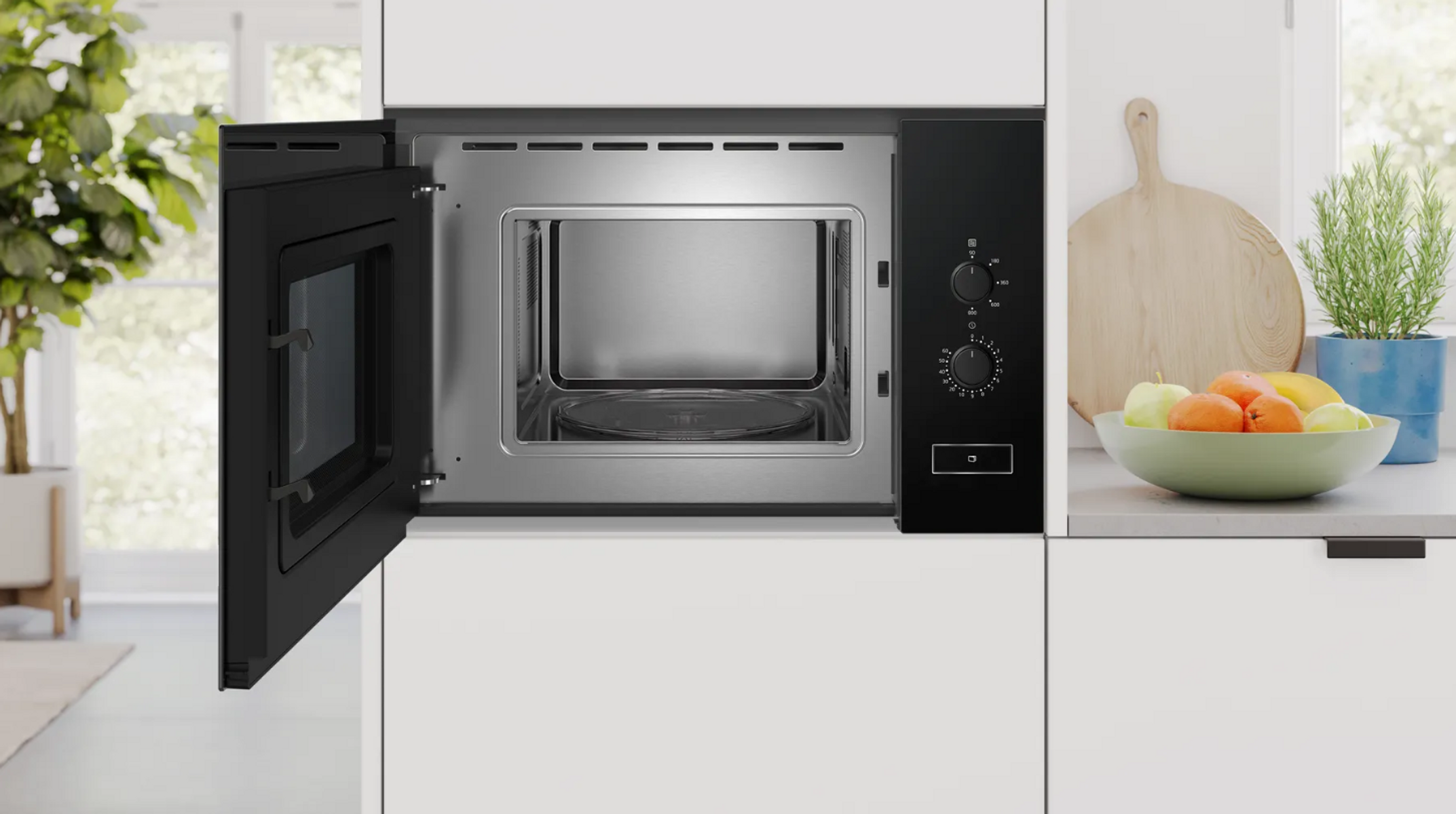 Kuchenka mikrofalowa, czarna z otwartymi drzwiami. Otoczenie kuchenne z miską owoców i deską do krojenia.