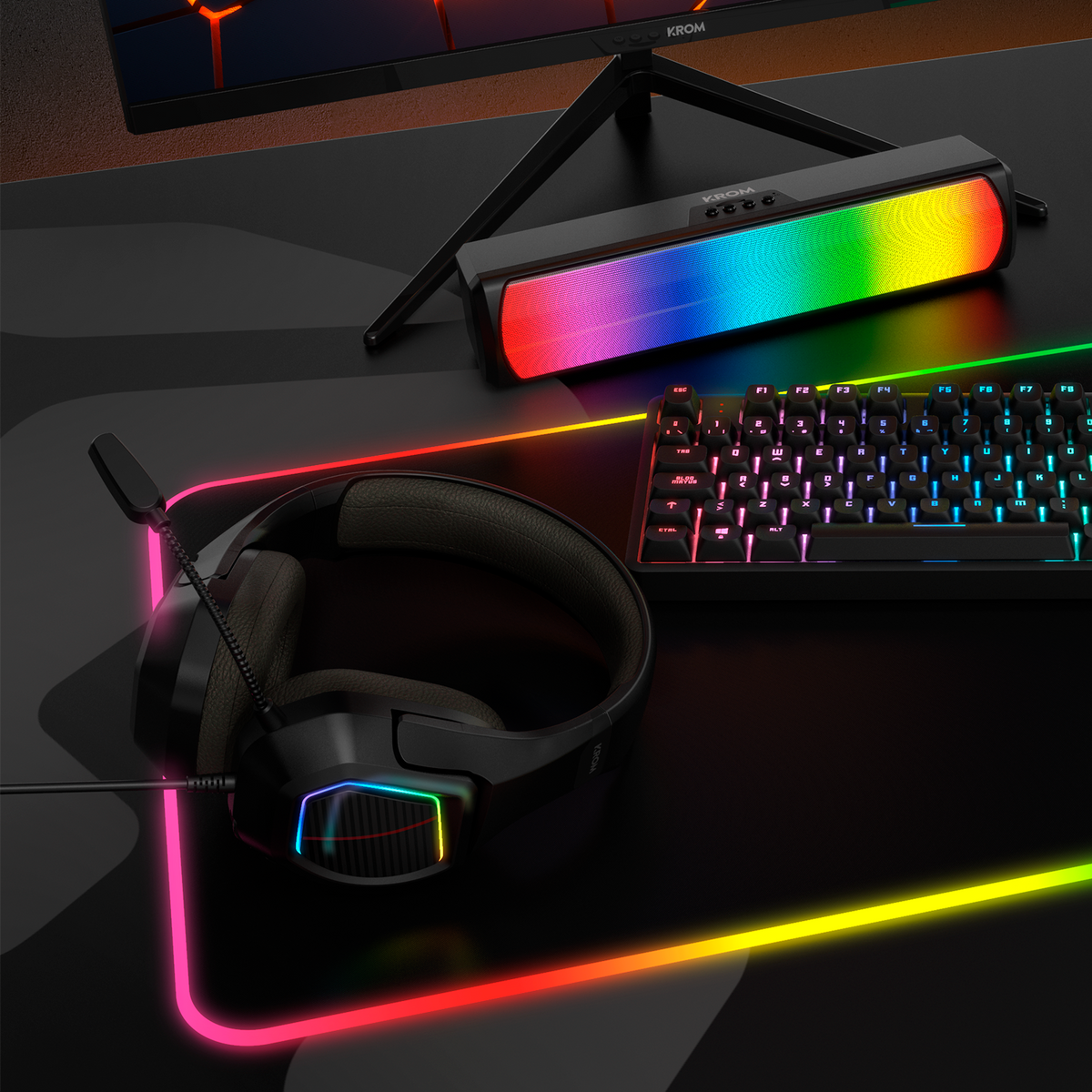 Configurazione gaming: tastiera RGB, altoparlante, tappetino e cuffie su superficie nera, logo KROM visibile.