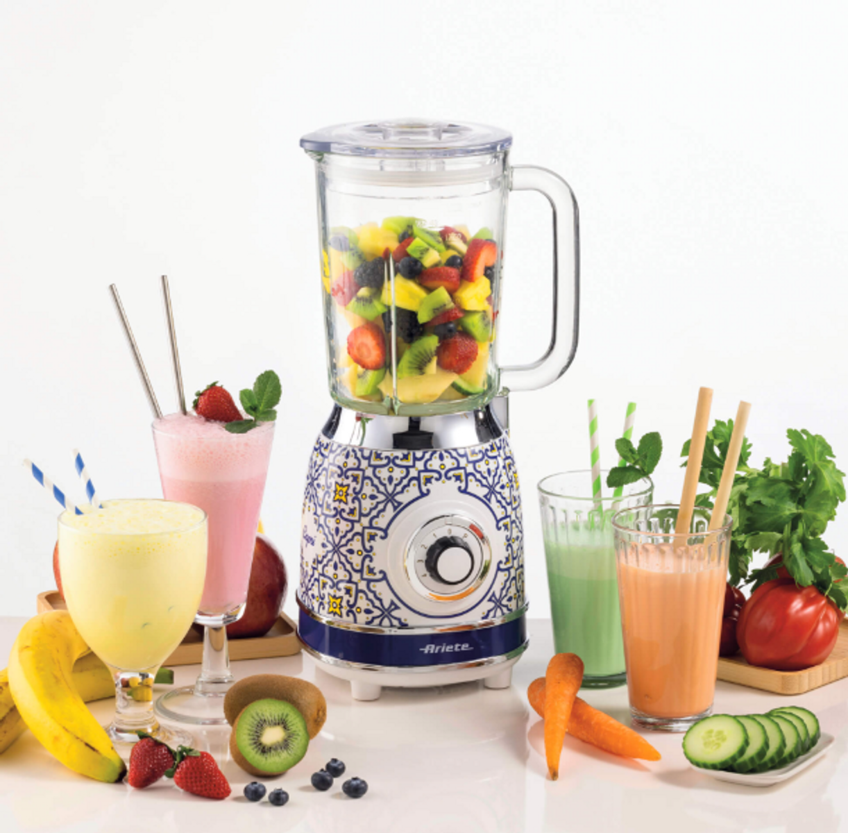Un frullatore con frutta è circondato da frullati, frutta e verdura su una superficie bianca.