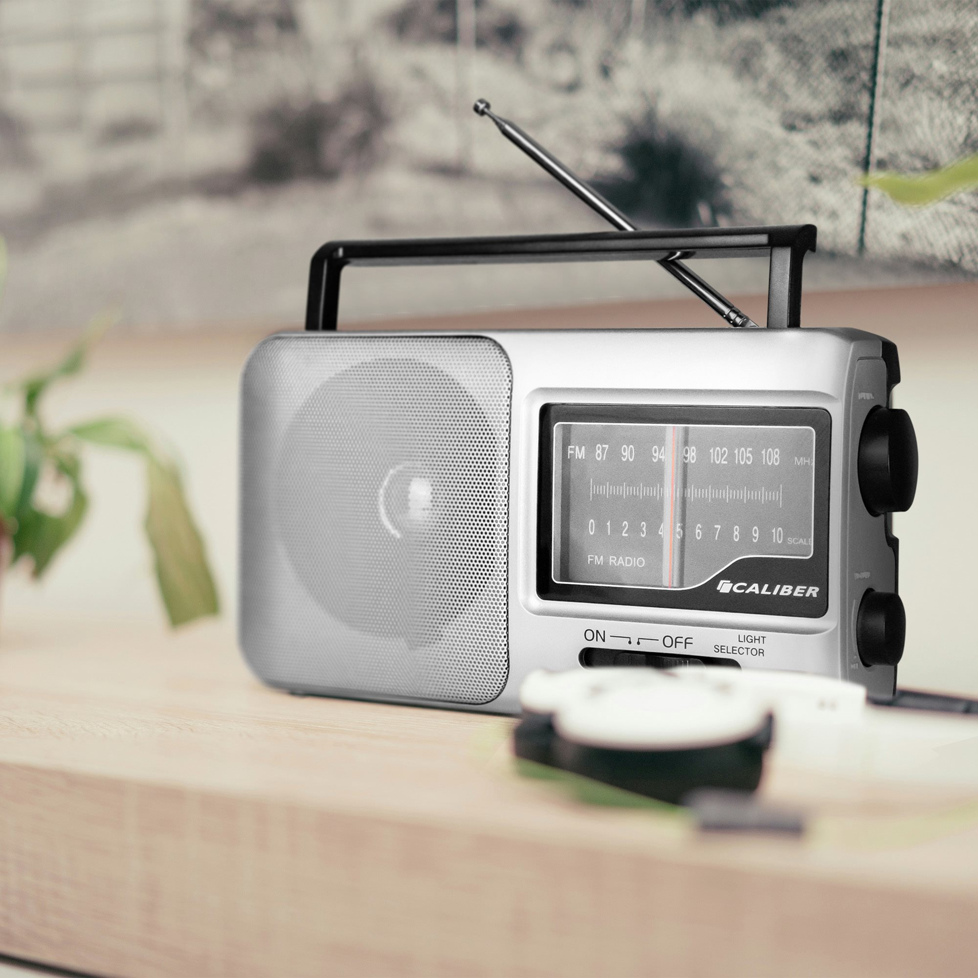 Silver Caliber radio on a wooden surface with a plant in the background.
