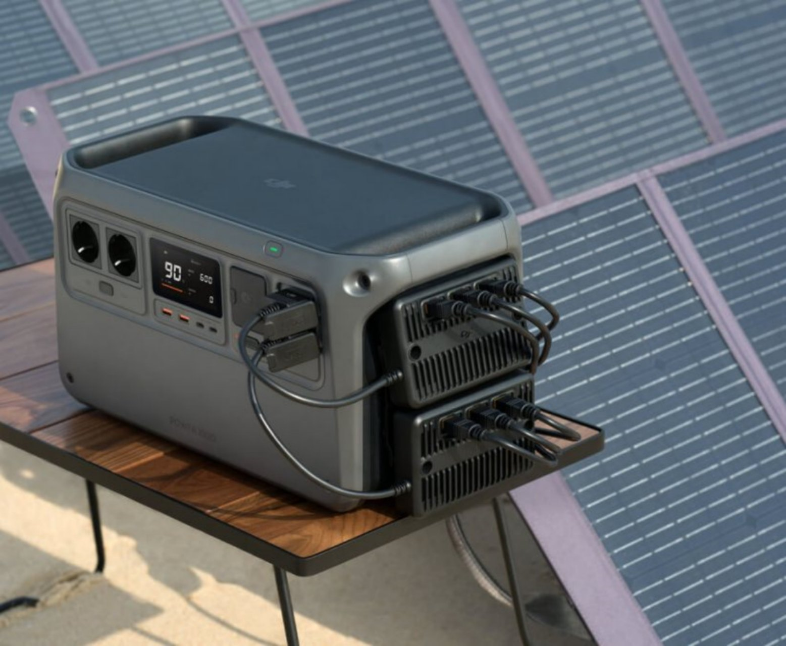Tragbarer Generator auf einem Tisch mit Sonnenkollektoren im Hintergrund. Anzeige zeigt 90% Ladung.