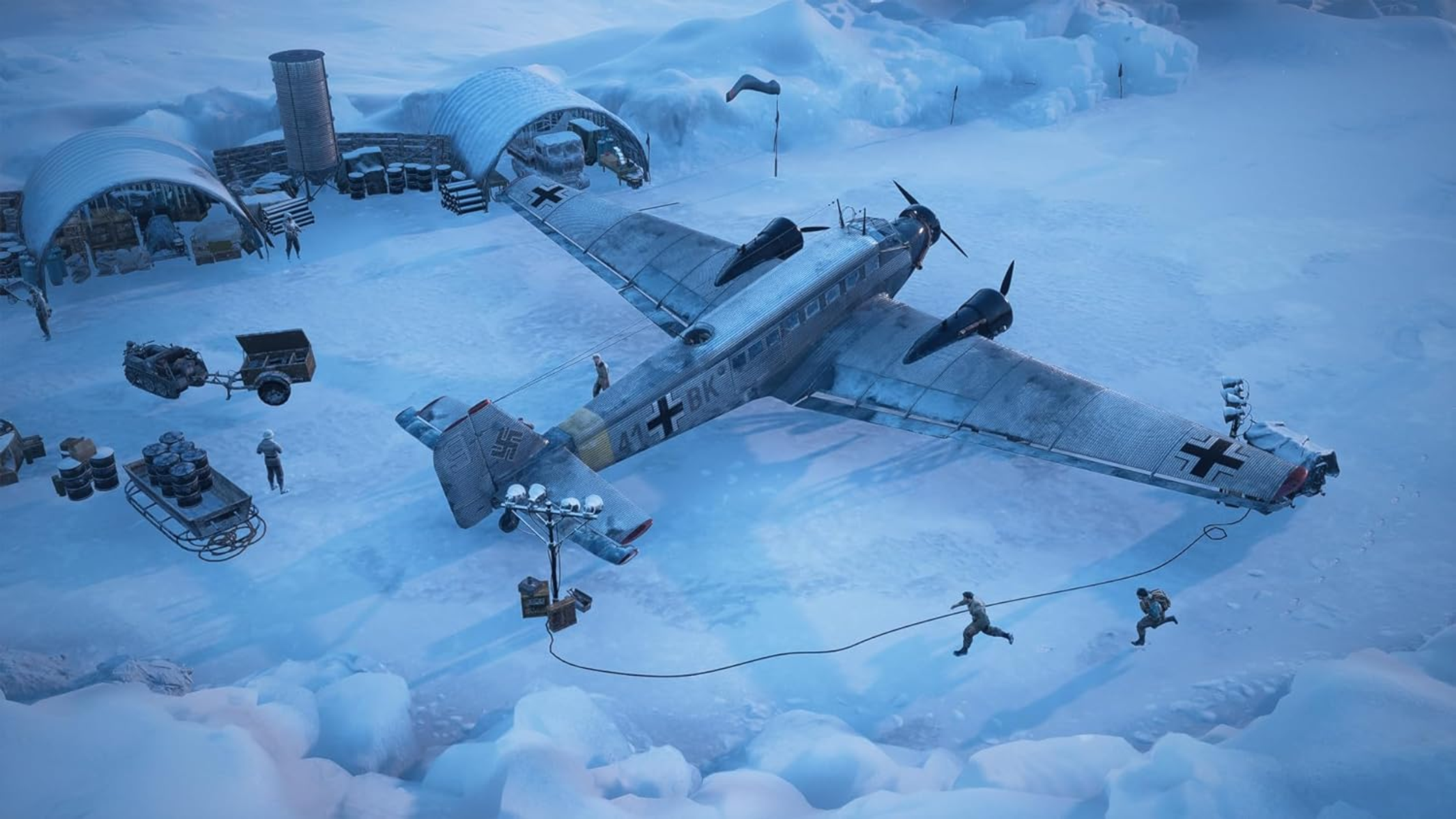 Vista aérea de un avión en la nieve, con edificios, personas y un remolque. La escena es fría.