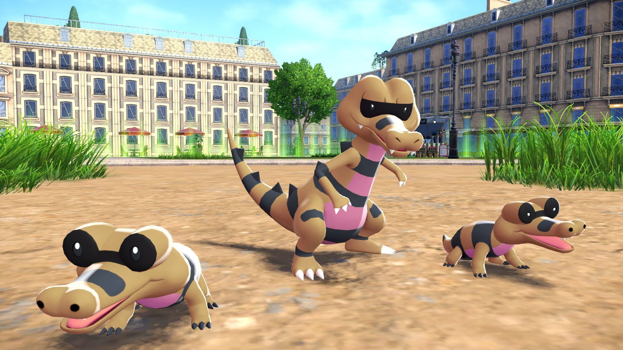 Trzy Pokémony podobne do krokodyli w parku. Budynki i drzewa w tle.