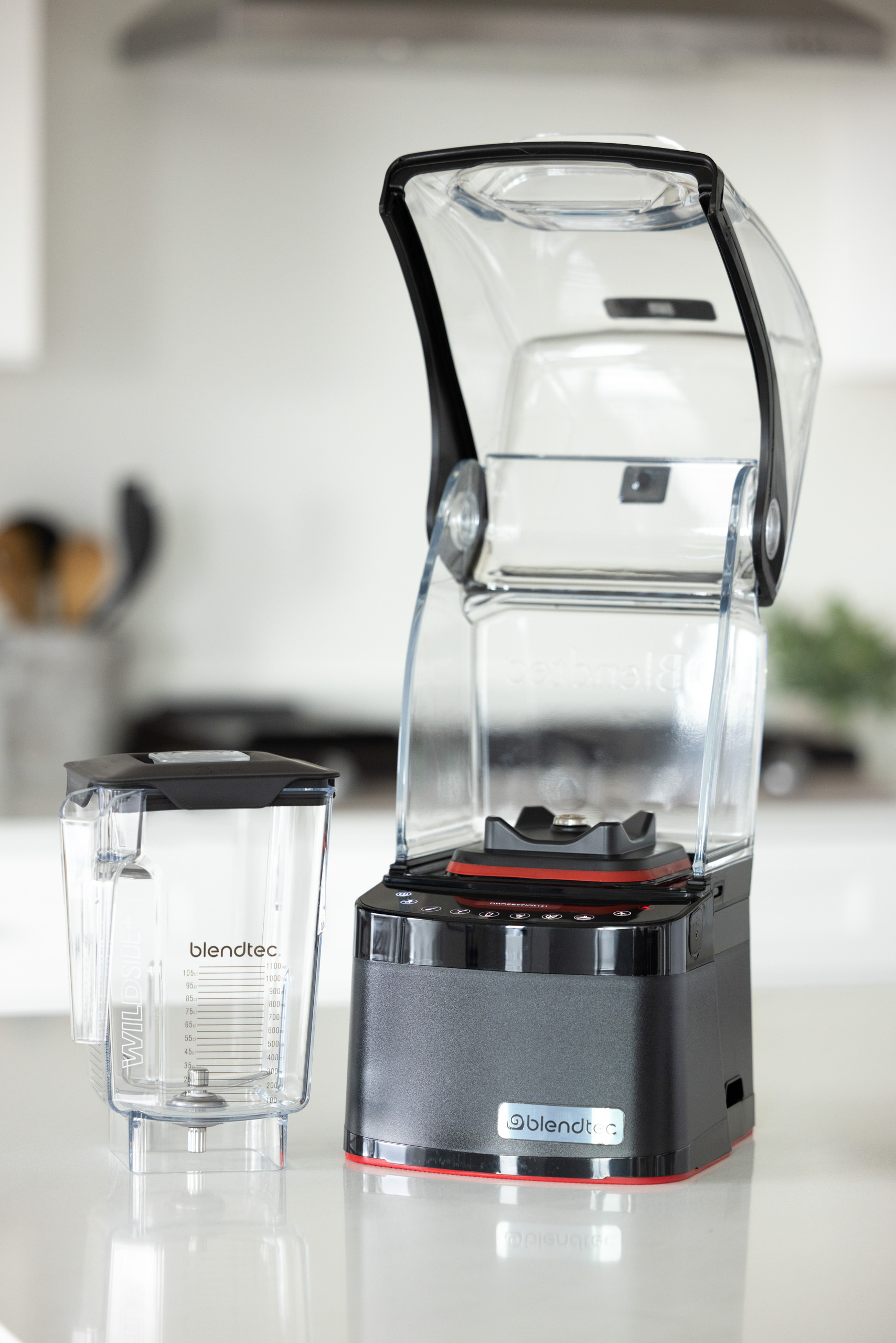 Frullatore Blendtec con contenitore e coperchio trasparenti, base nera, su superficie bianca.