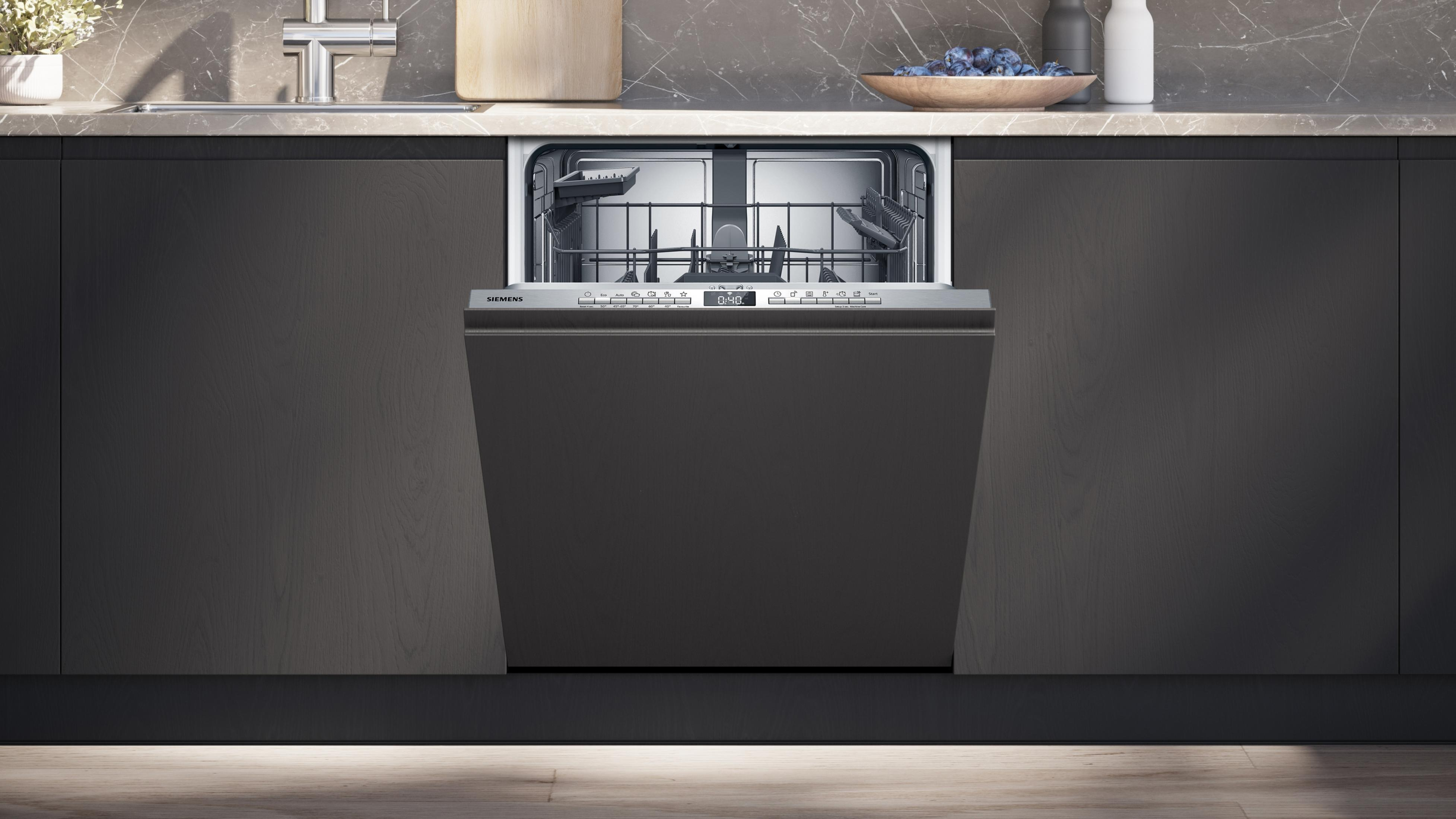 Una lavastoviglie grigio scuro aperta in una cucina con mobili scuri e un piano di lavoro grigio.