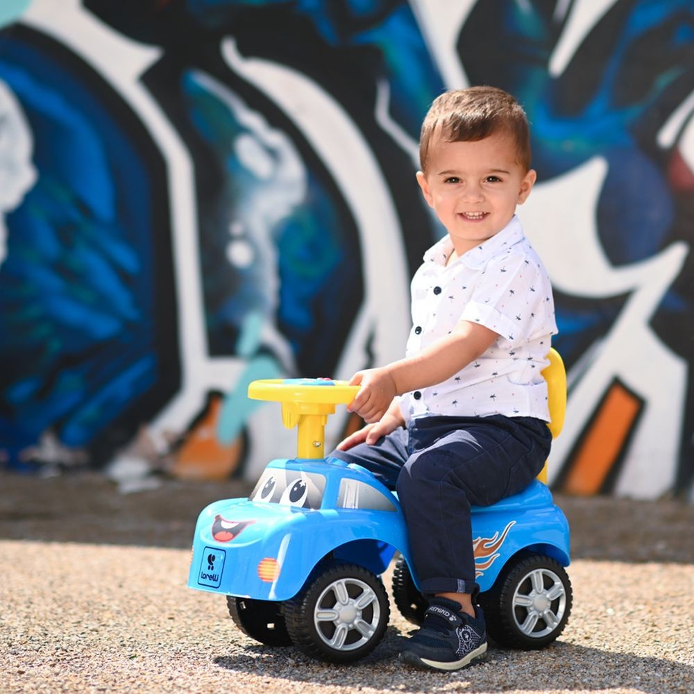 Niño pequeño feliz en coche de juguete azul sonriendo, con fondo de grafiti.
