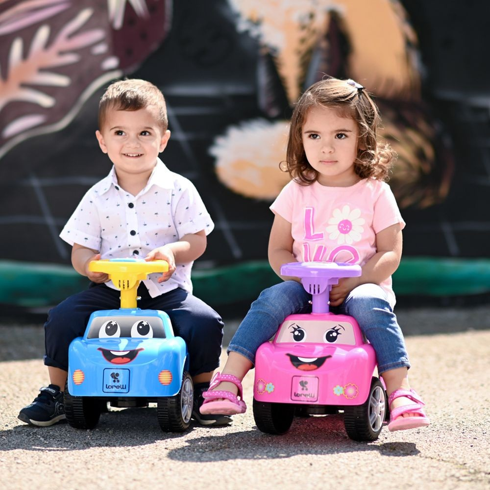 Dos niños montados en coches de juguete, uno azul, otro rosa, con sonrisas.