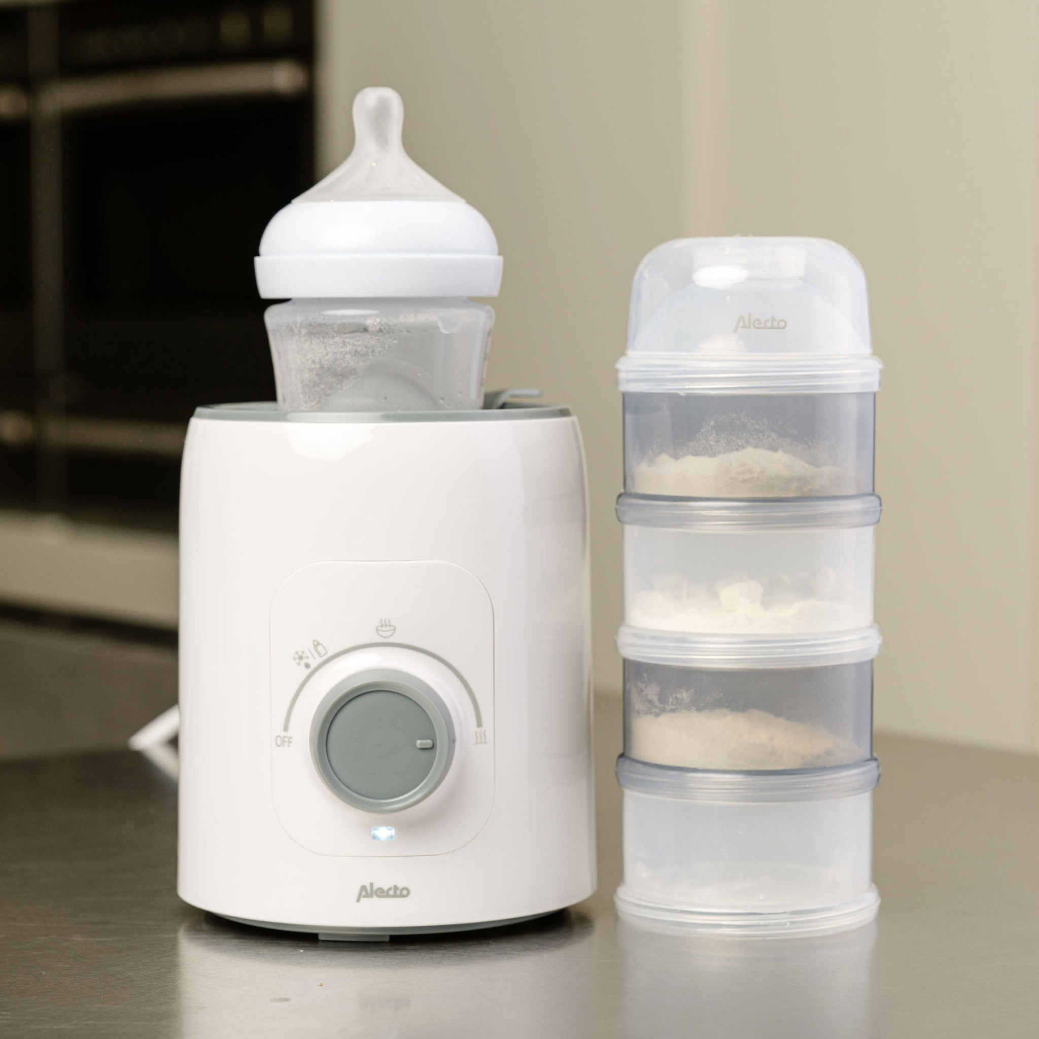 A baby bottle warmer with a bottle and formula containers. A gray dial is visible.