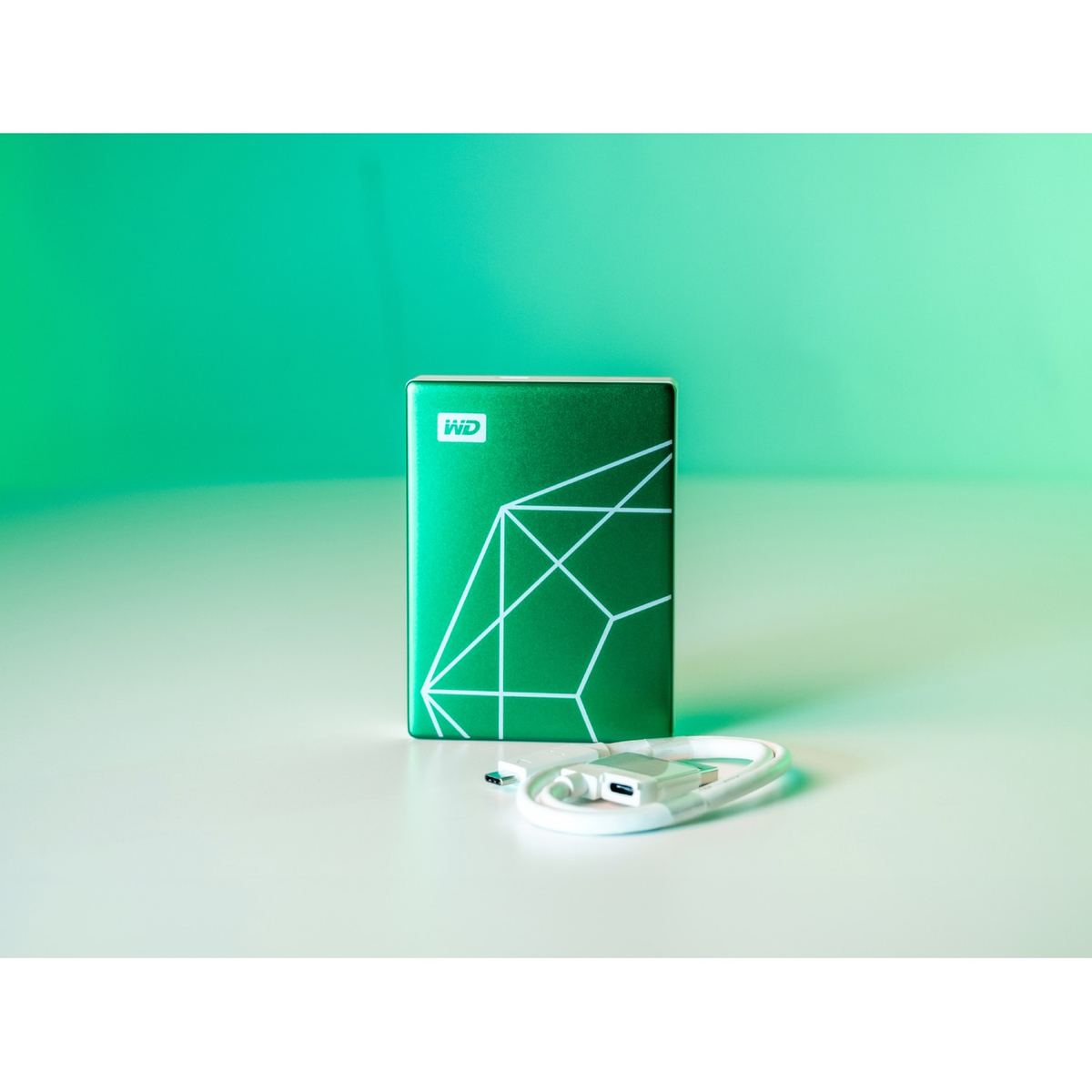 Zielony dysk twardy z białym geometrycznym wzorem i kablem USB na białej powierzchni.