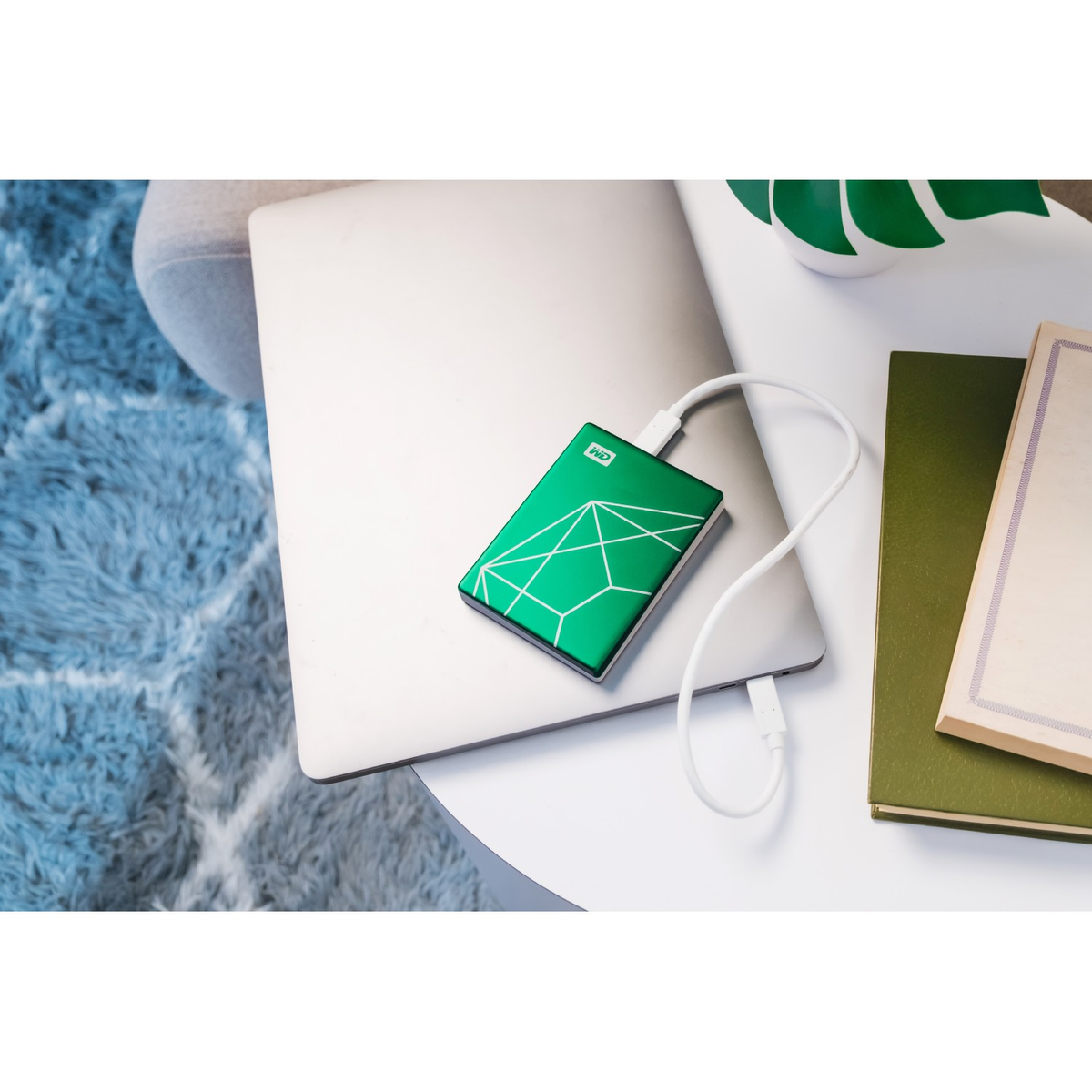 Zielony zewnętrzny dysk twardy podłączony do srebrnego laptopa białym kablem.