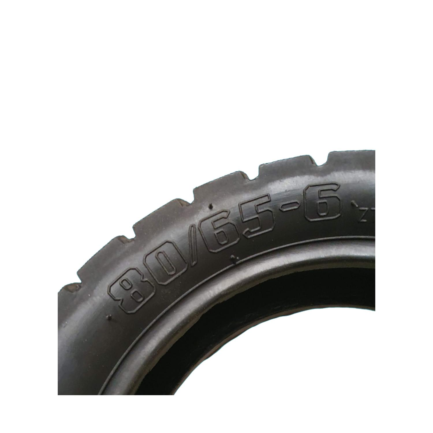 Primer plano de neumático de motocicleta. Neumático negro con texto blanco: 80/65-6. Fondo blanco.