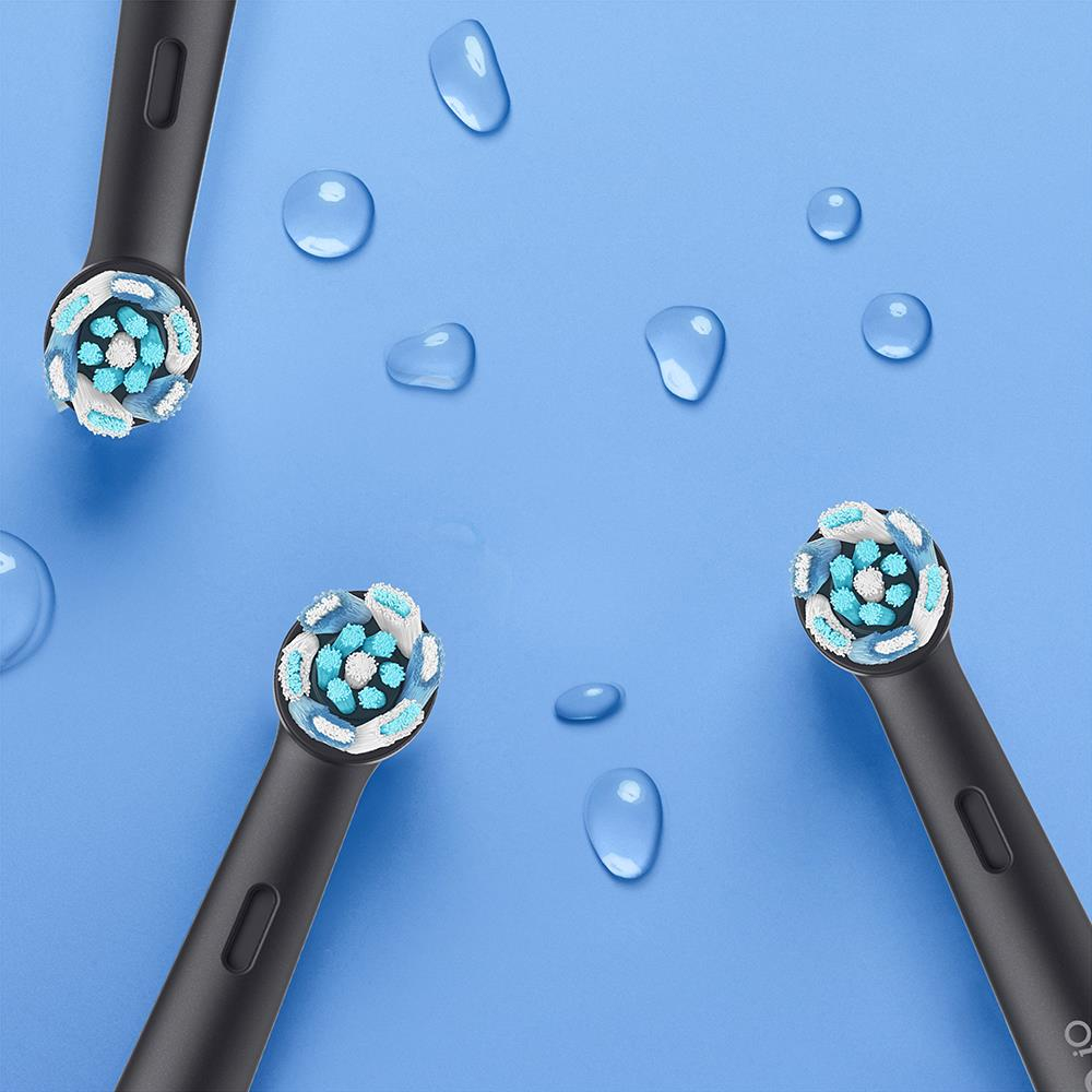 Tre testine di spazzolino nere con setole blu e bianche, su sfondo blu, gocce d'acqua.
