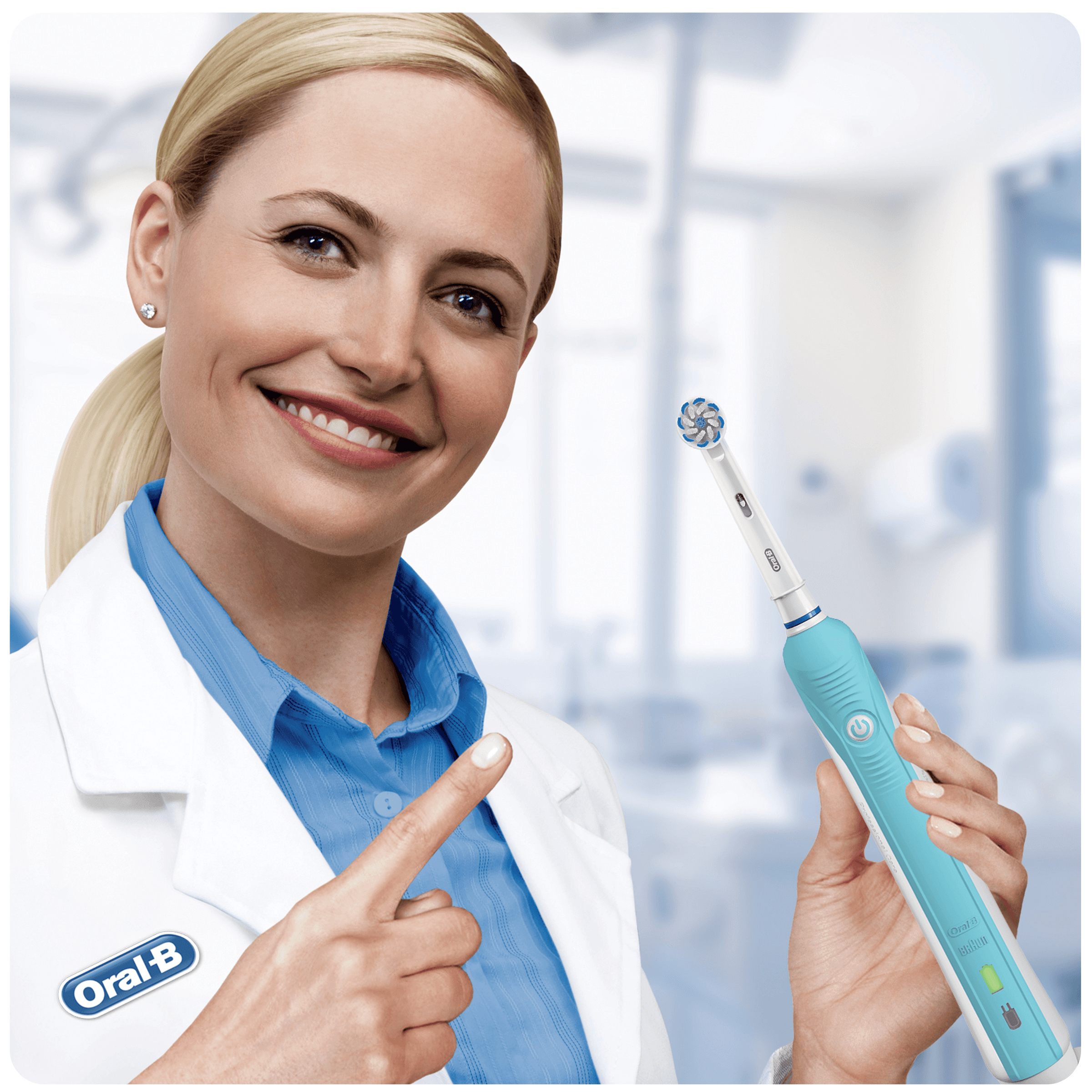 Una mujer sonriente con una bata de laboratorio sostiene un cepillo de dientes eléctrico, señalándolo con la otra mano.