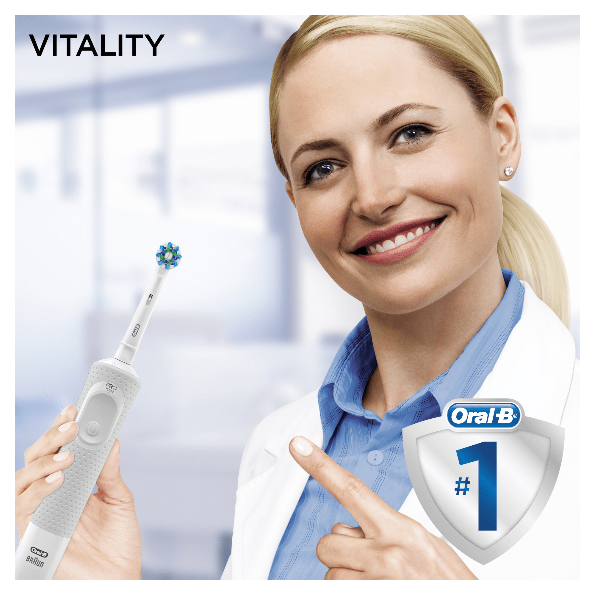 Kobieta w kitlu uśmiecha się i wskazuje na szczoteczkę Oral-B z widocznym logo marki.