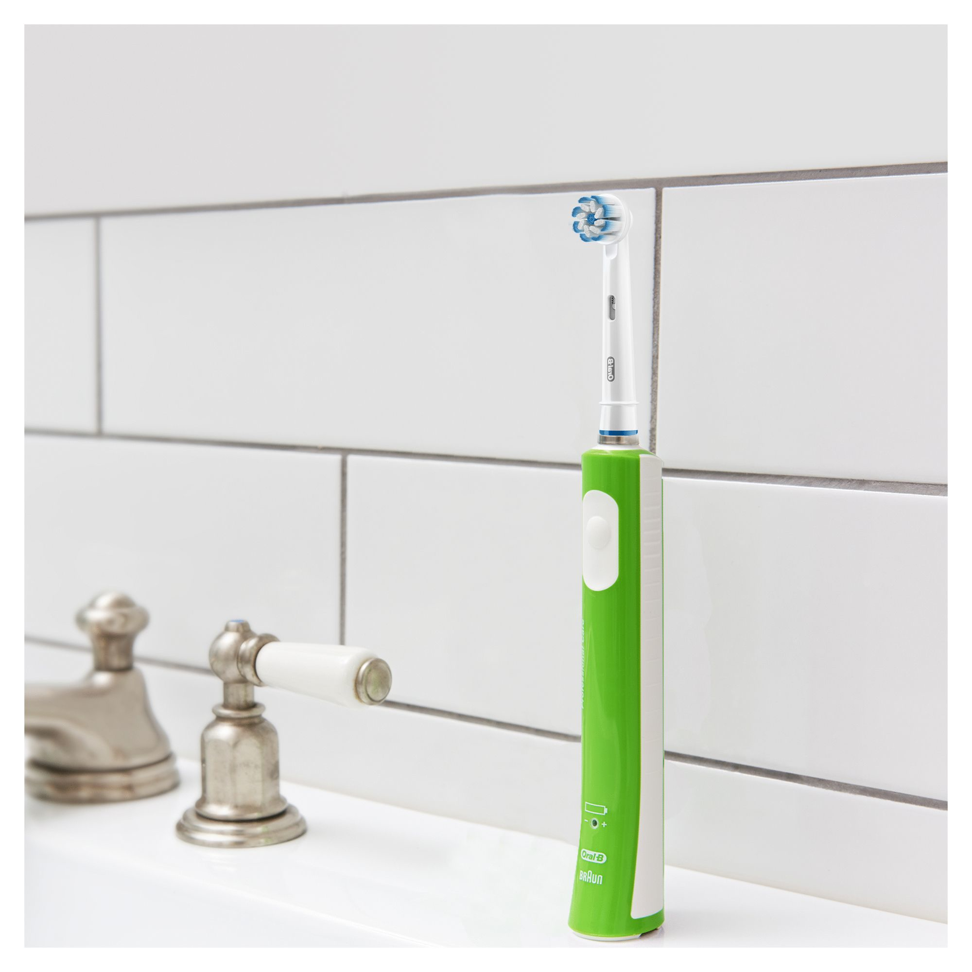 Eine grün-weiße elektrische Zahnbürste steht auf einem weißen Waschbecken neben einem Chrom-Wasserhahn.
