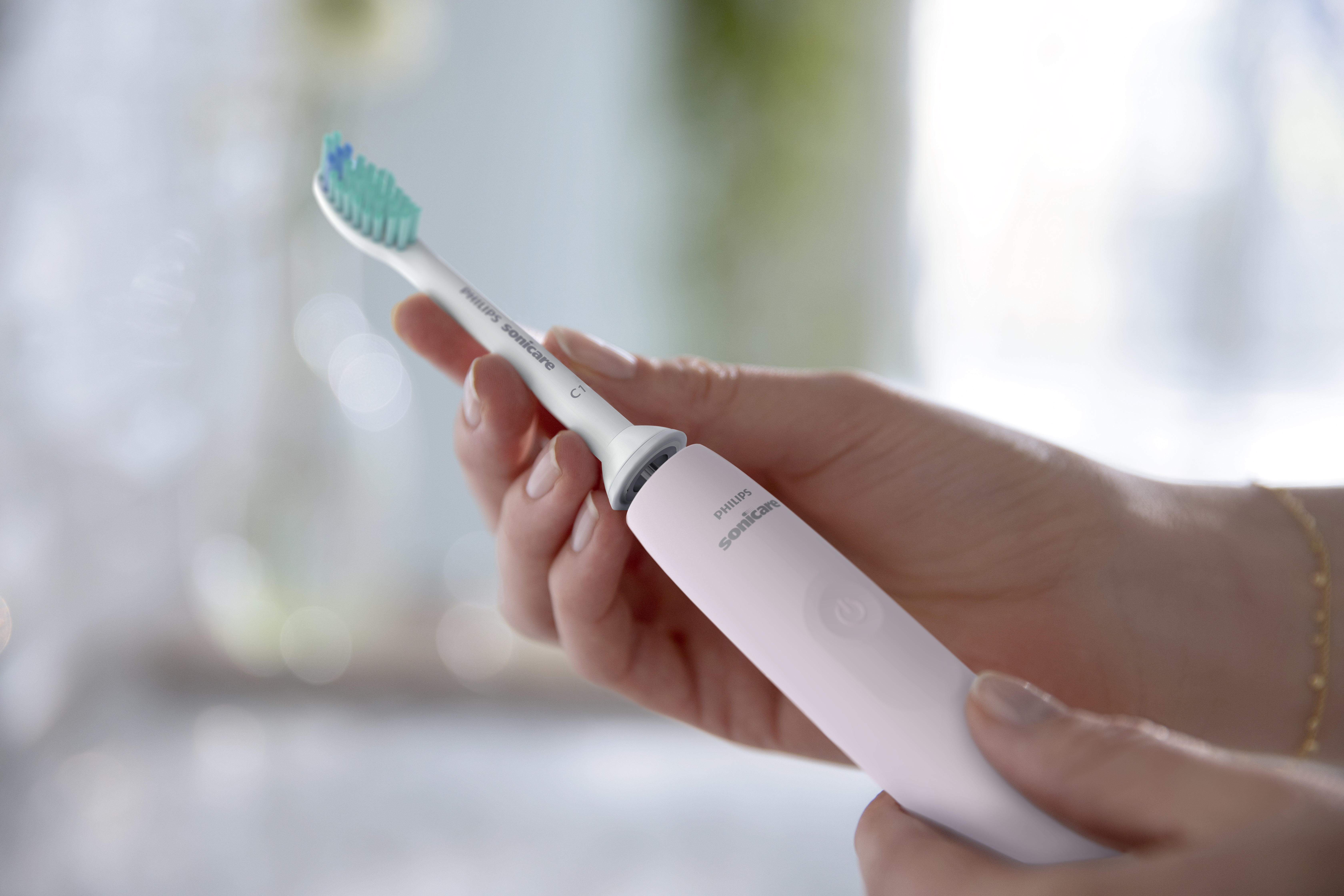 Ręce trzymające różową szczoteczkę Philips Sonicare. Zielone/niebieskie włosie, biały uchwyt.