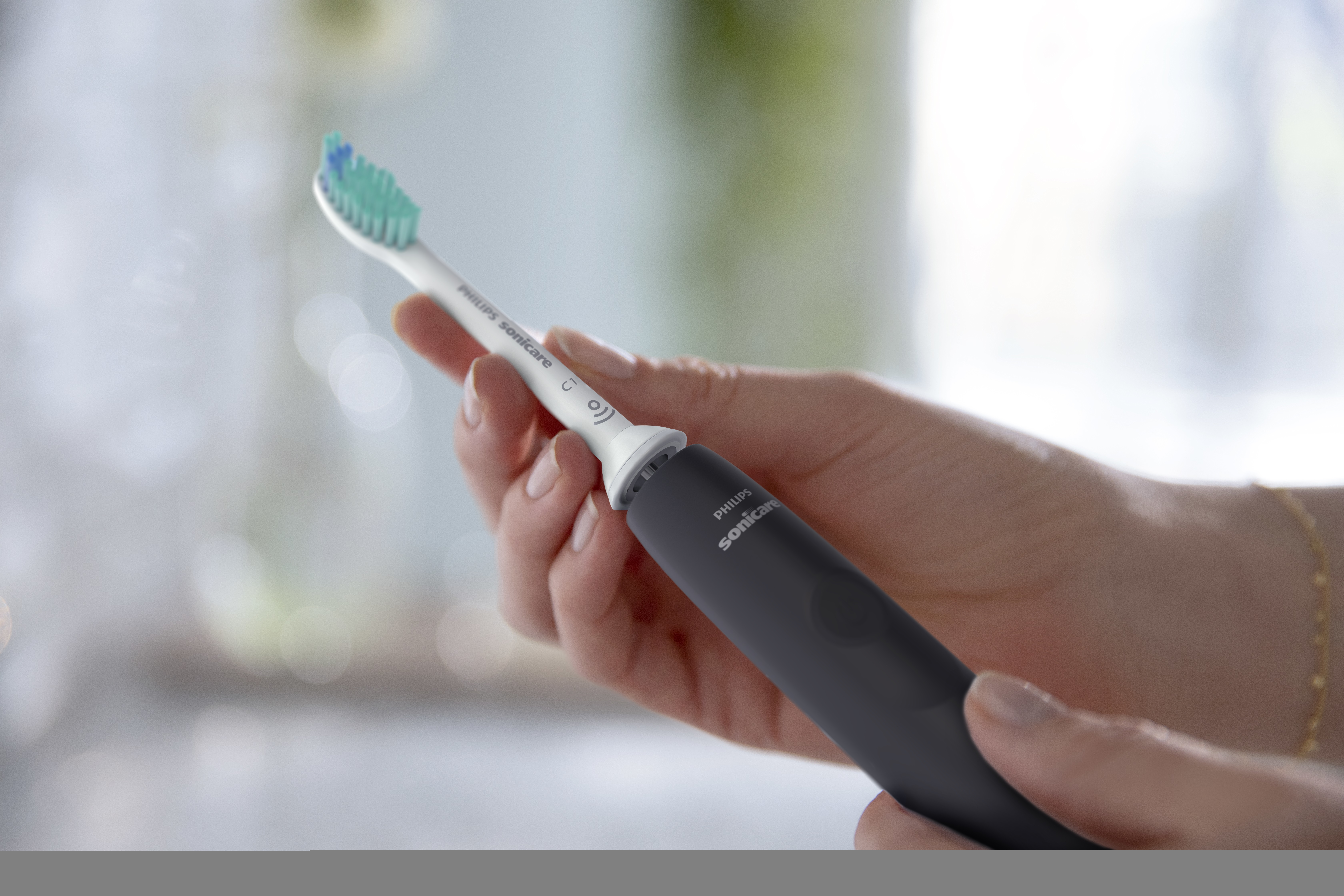 Osoba trzymająca szczoteczkę Philips Sonicare, szarą z główką.