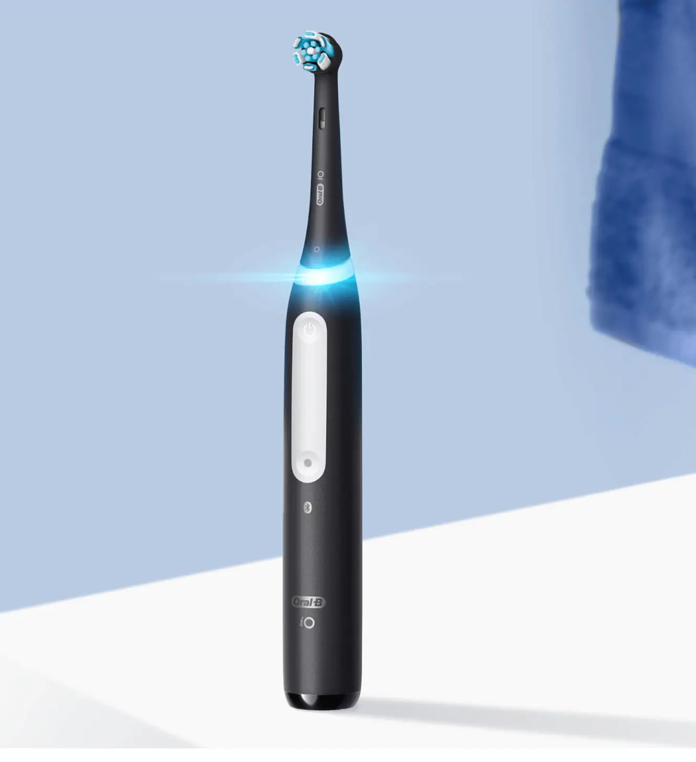 Czarna elektryczna szczoteczka do zębów z białym przyciskiem zasilania, niebieskim światłem i logo Oral-B.