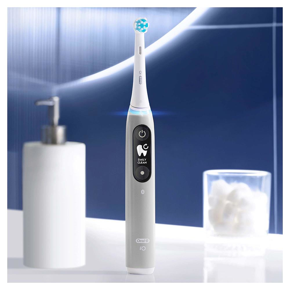 Cepillo de dientes eléctrico, gris, con pantalla y botones, en un baño.