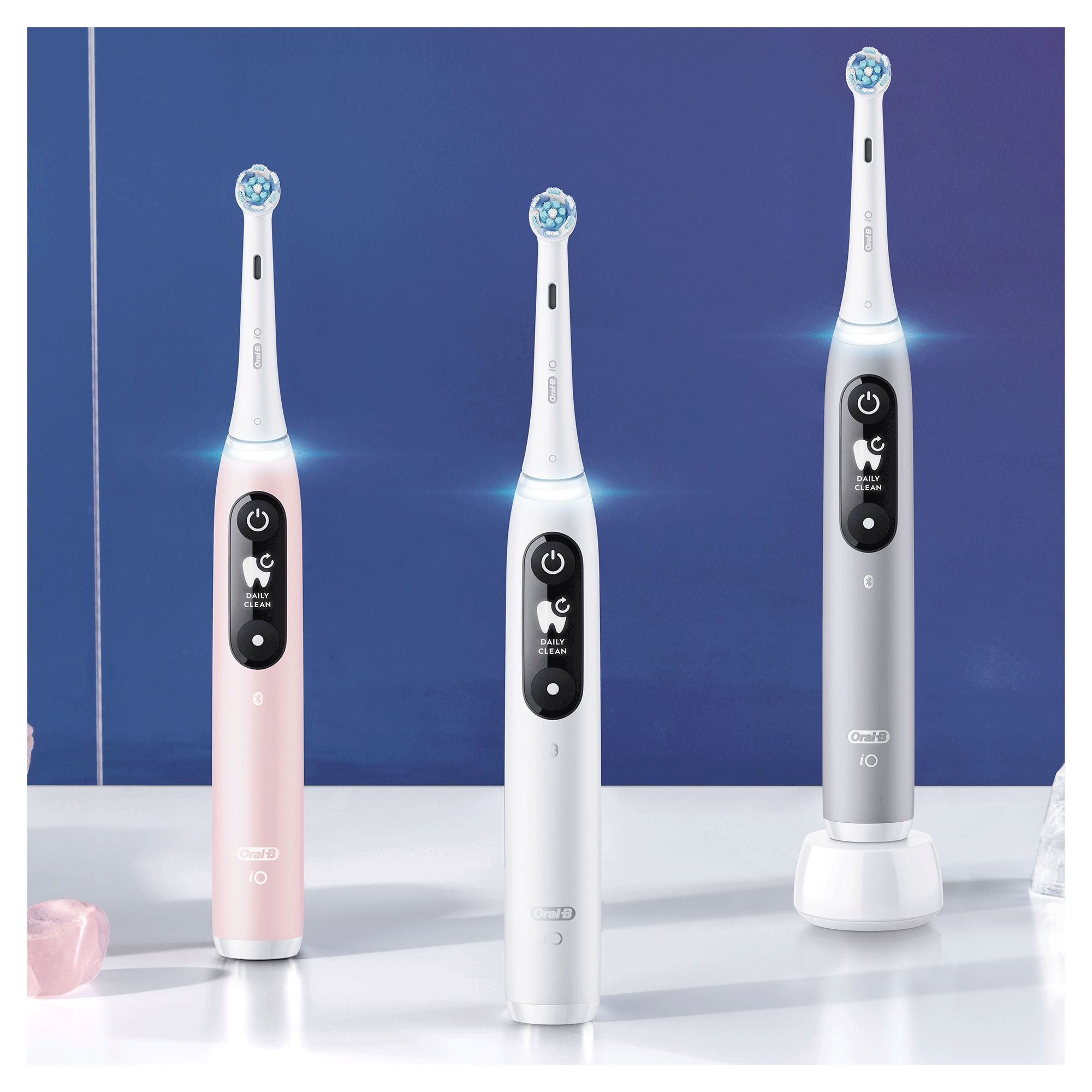 Tres cepillos de dientes eléctricos sobre una superficie blanca. Rosa, blanco y gris.