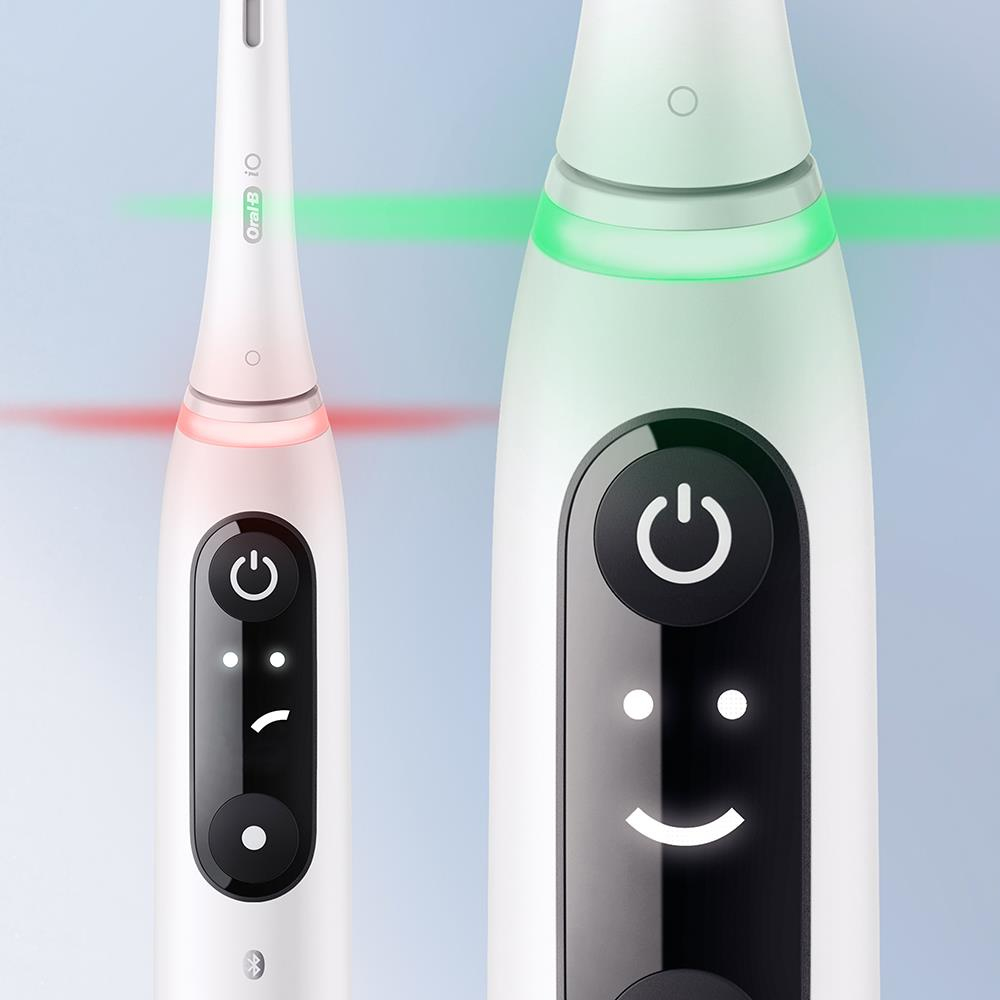 Dos cepillos de dientes eléctricos blancos, uno con luz roja, otro verde. Ambos tienen botón de encendido y una carita sonriente.