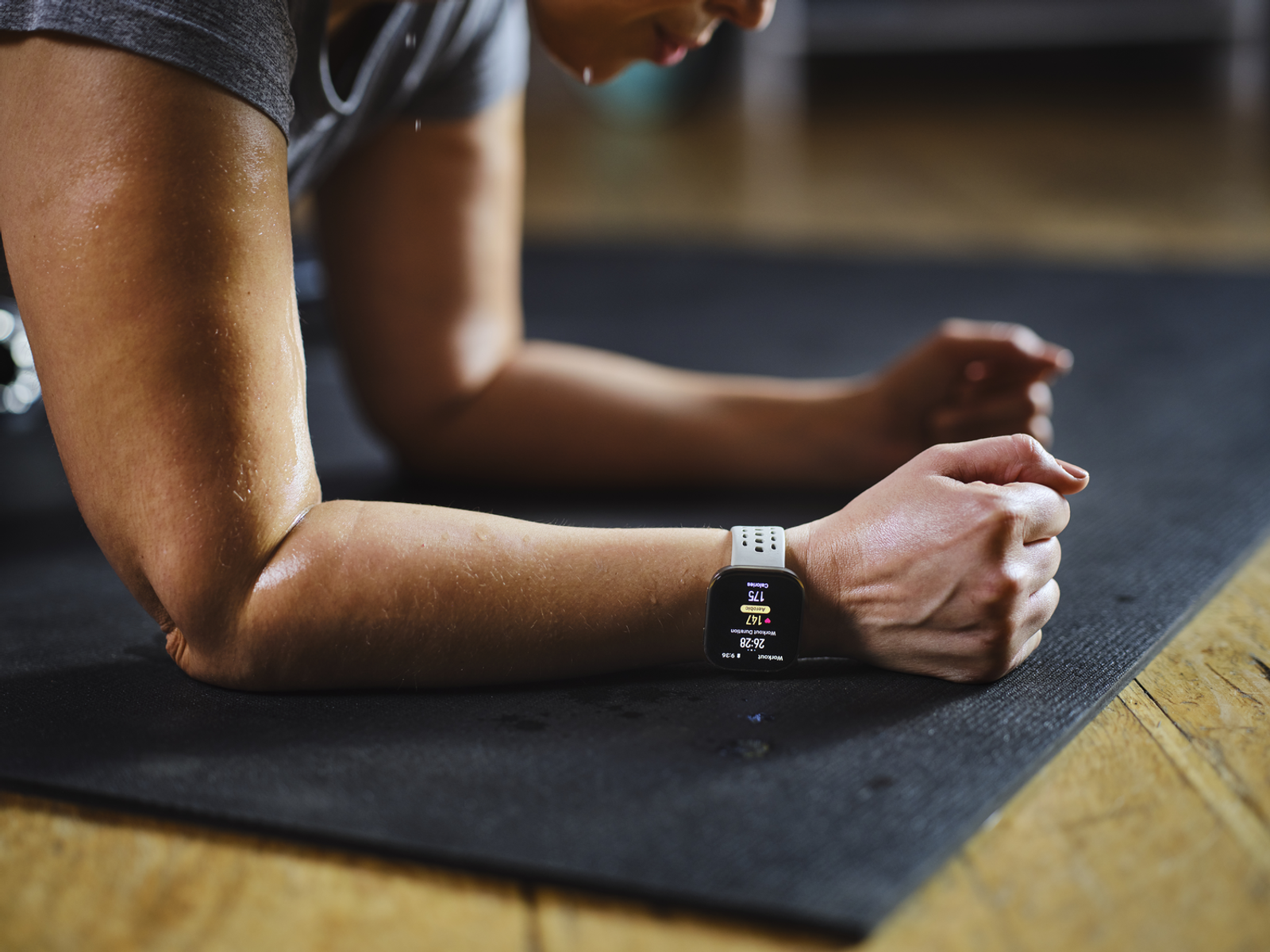 Kobieta w pozycji deski, nosząca smartwatch, który wyświetla dane treningu na ekranie.