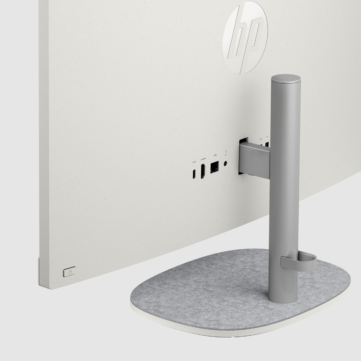 Parte trasera de un monitor blanco, con puertos y un soporte sobre una base de fieltro gris.