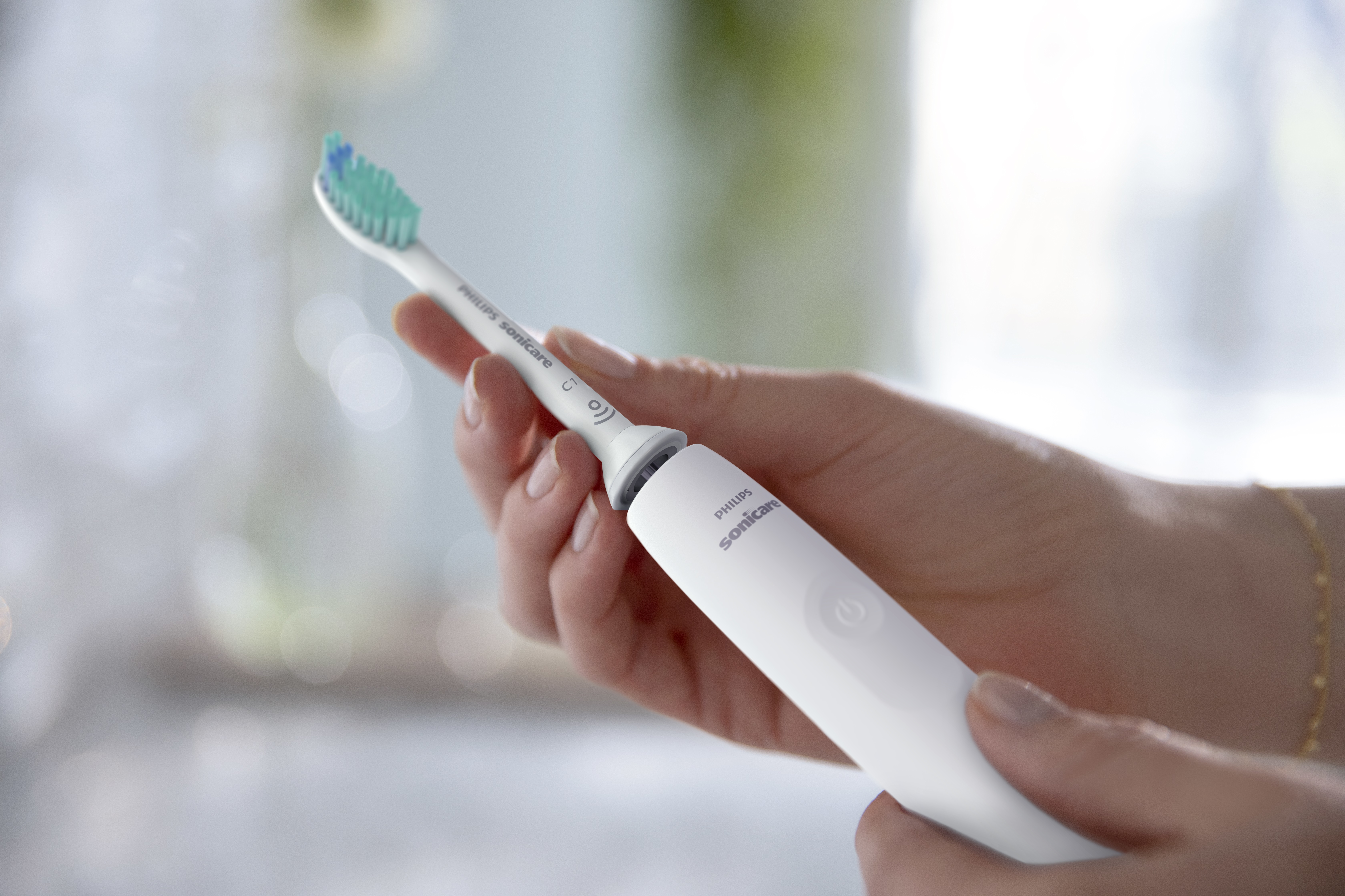 Osoba trzyma białą szczoteczkę Philips Sonicare. Szczoteczka ma zieloną i niebieską główkę.