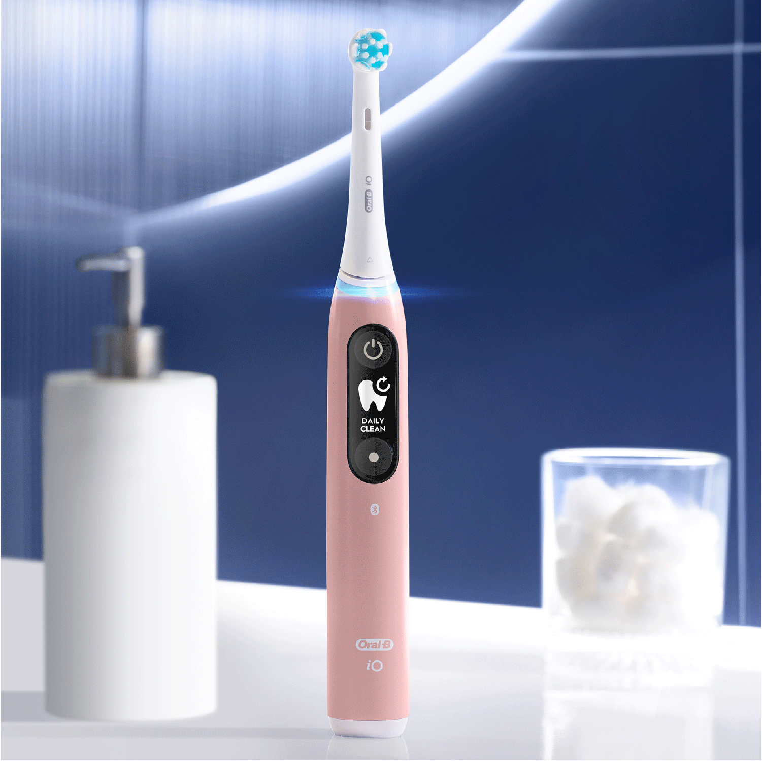 Roze Oral-B iO elektrische tandenborstel met een schone kop, naast een dispenser en wattenbollen.