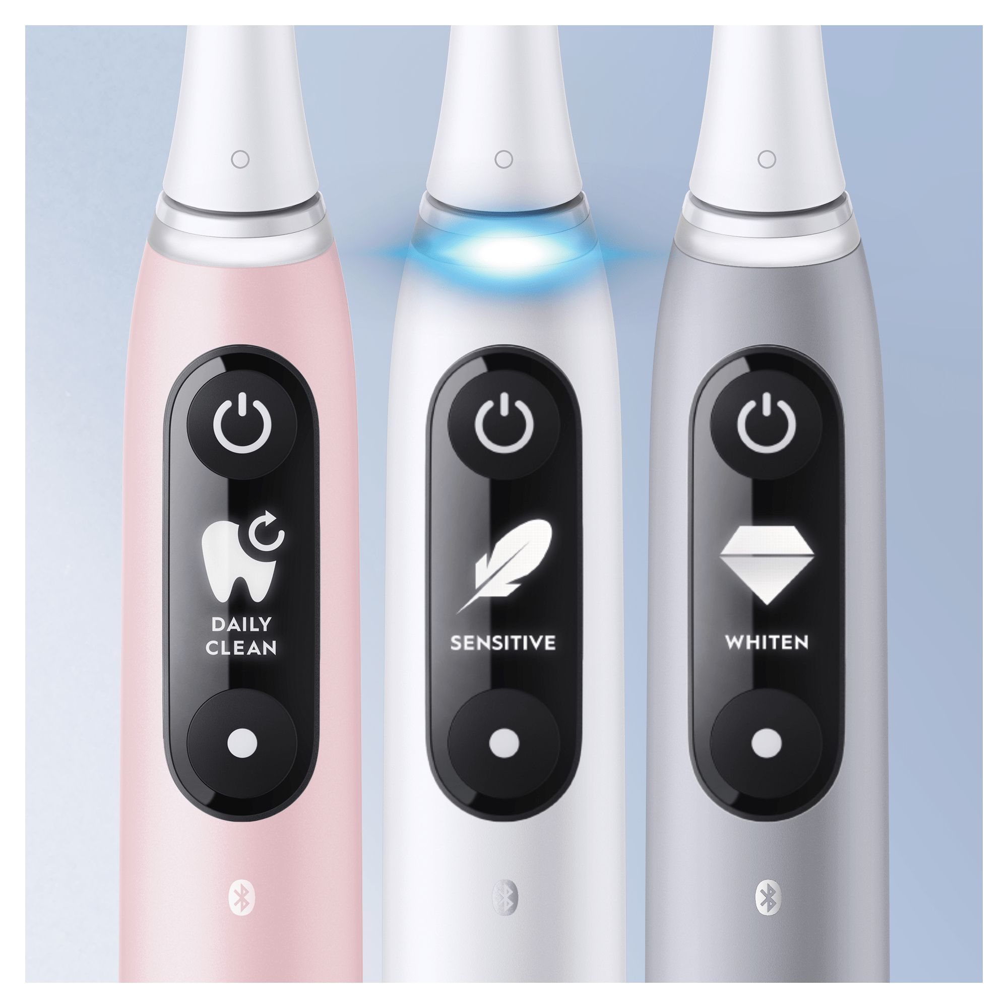Three electric toothbrushes, pink, white, and gray, with power buttons, on blue backdrop.