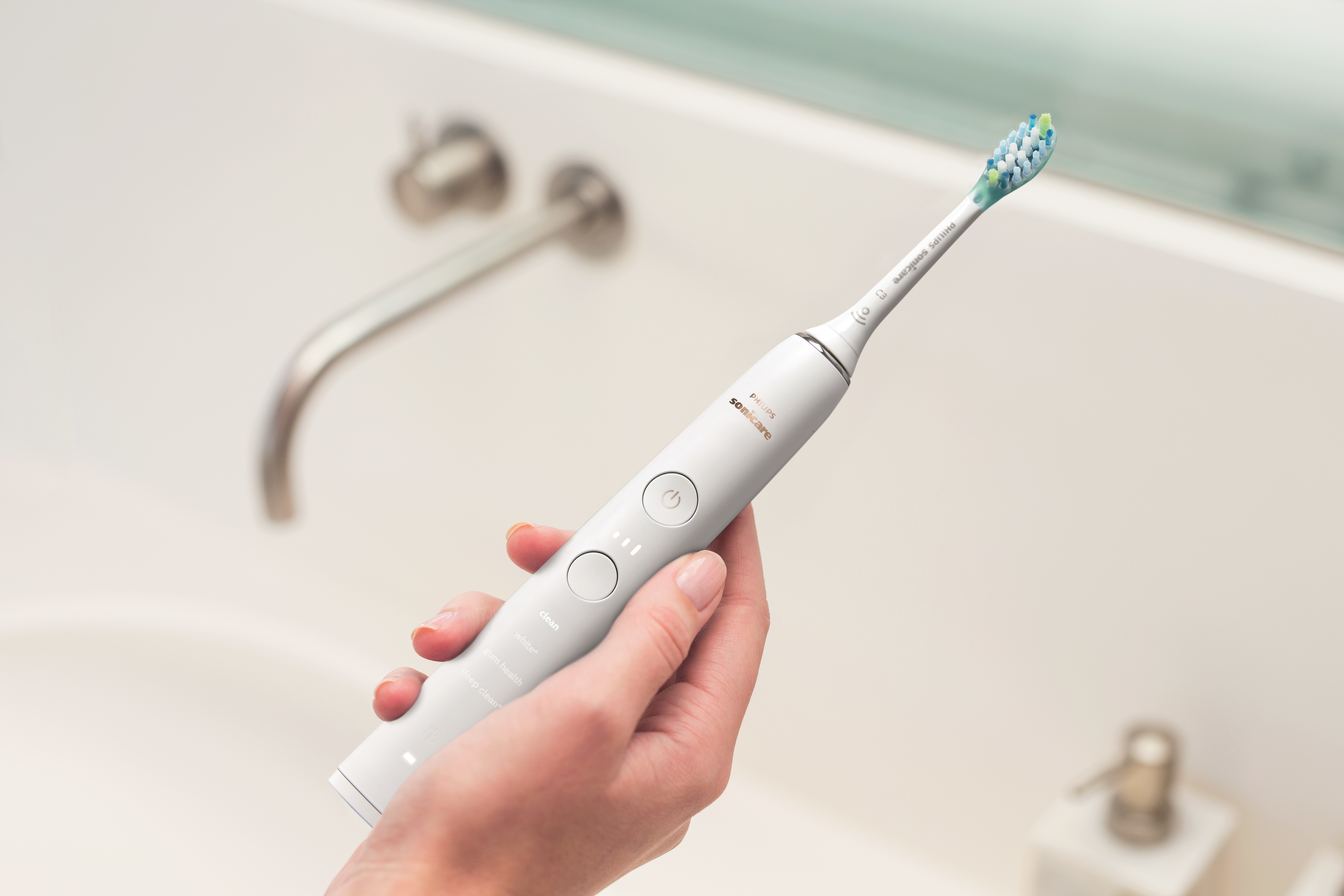 Una mano che tiene uno spazzolino Philips Sonicare bianco vicino a un rubinetto.