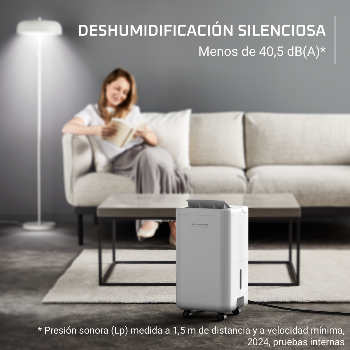 Donna che legge, seduta vicino a un deumidificatore bianco. Testo: "Deumidificazione silenziosa, meno di 40,5 dB".