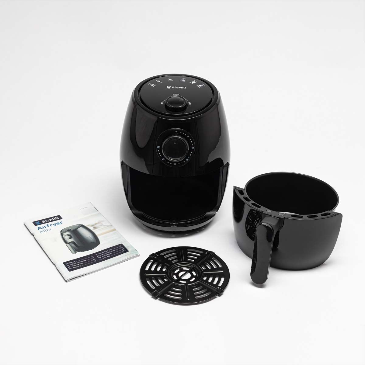 Zwarte airfryer met accessoires en een brochure op een wit oppervlak.