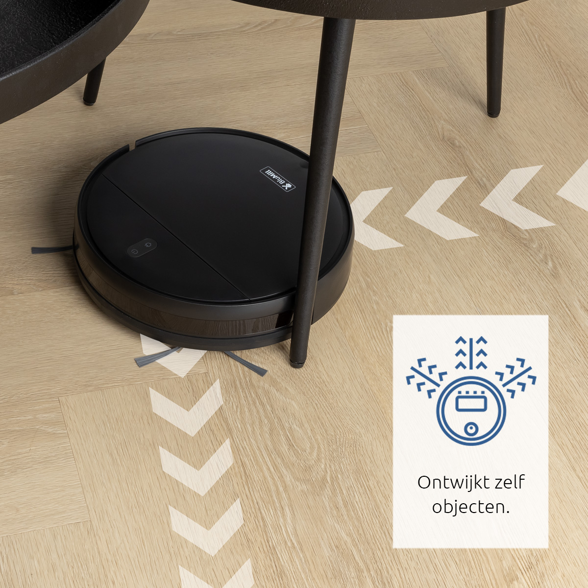 Un aspirateur robot noir sur un sol en bois, à côté d'une table.