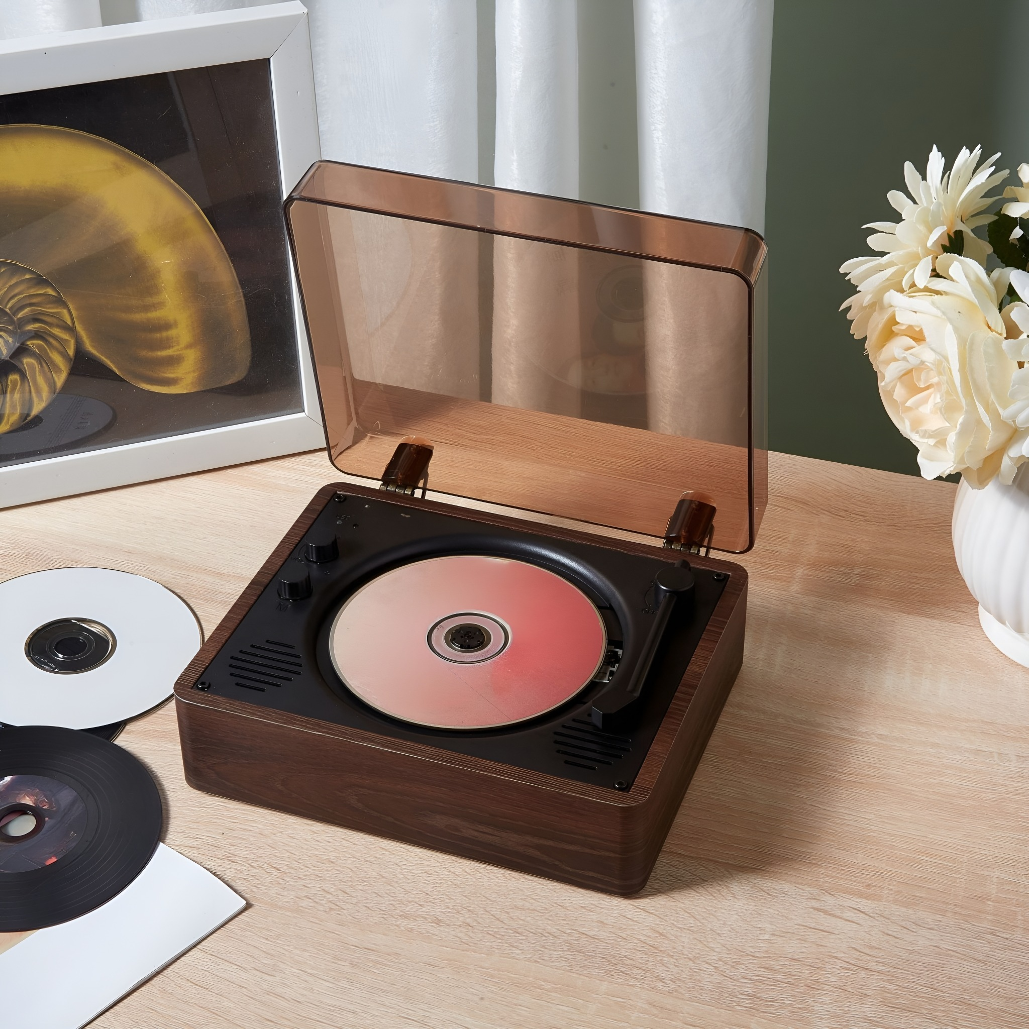 Ein Vintage-Plattenspieler mit transparentem Deckel auf einem Holztisch. Daneben eine weiße Vase mit Blumen.