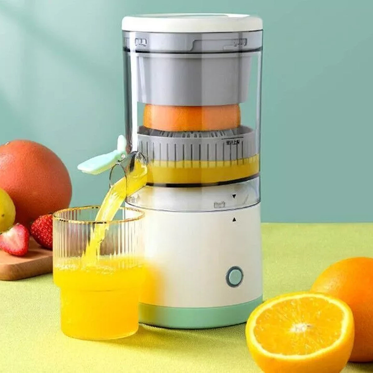 Eine Orangensaftmaschine mit einem Glas Saft, das gegossen wird, Orangen und Erdbeeren auf einer grünen Oberfläche.
