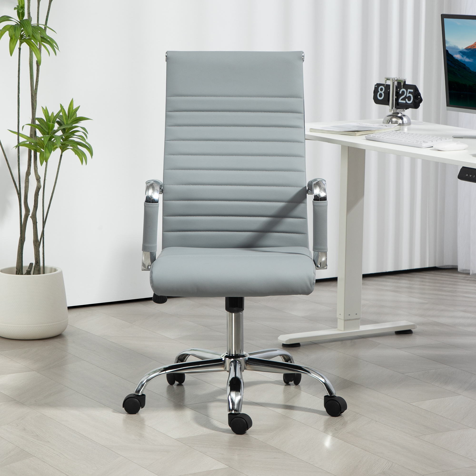 Una silla de oficina gris con respaldo alto y brazos cromados. Está frente a un escritorio blanco y una planta.
