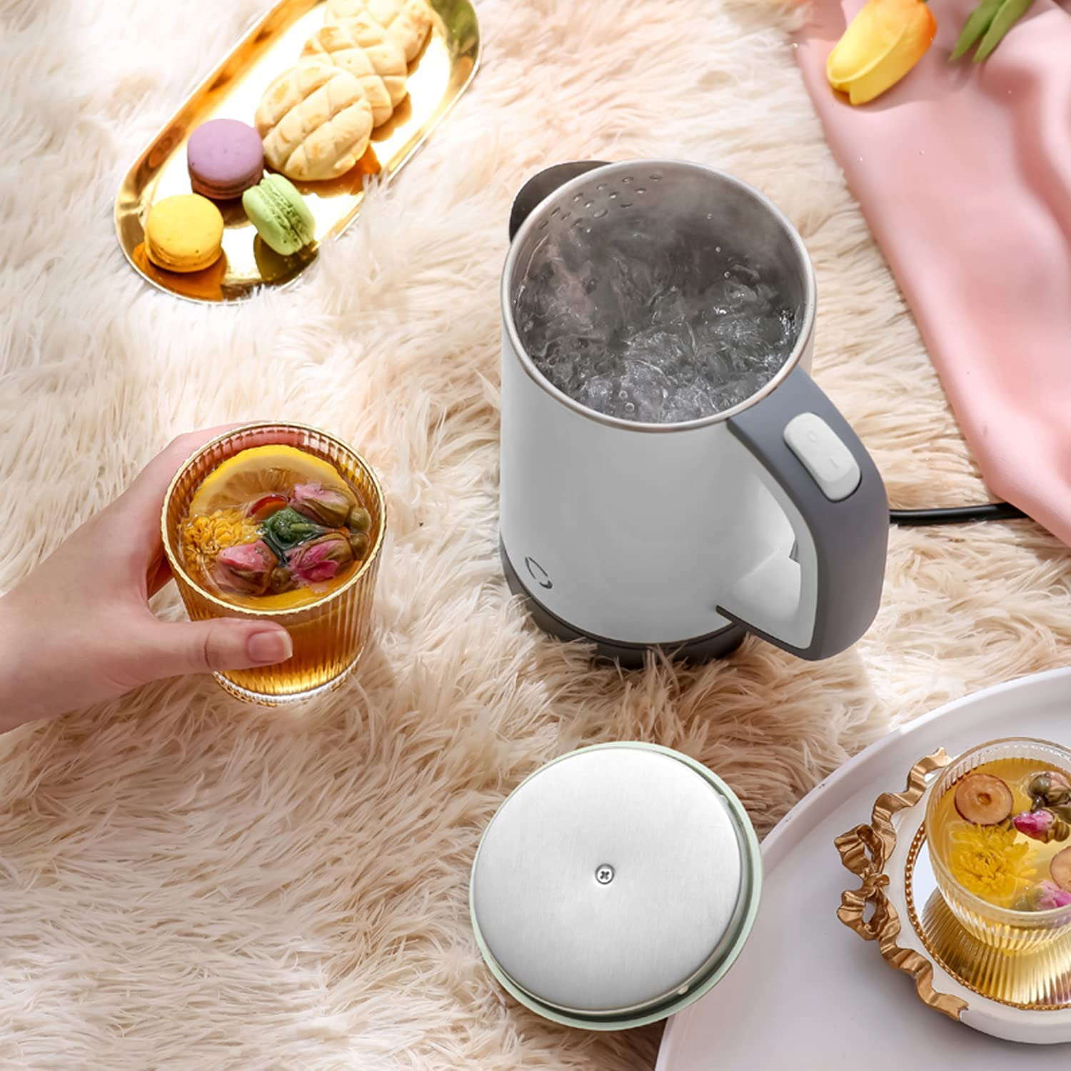Wasserkocher auf einer flauschigen Oberfläche mit einer Tasse Tee und Snacks.
