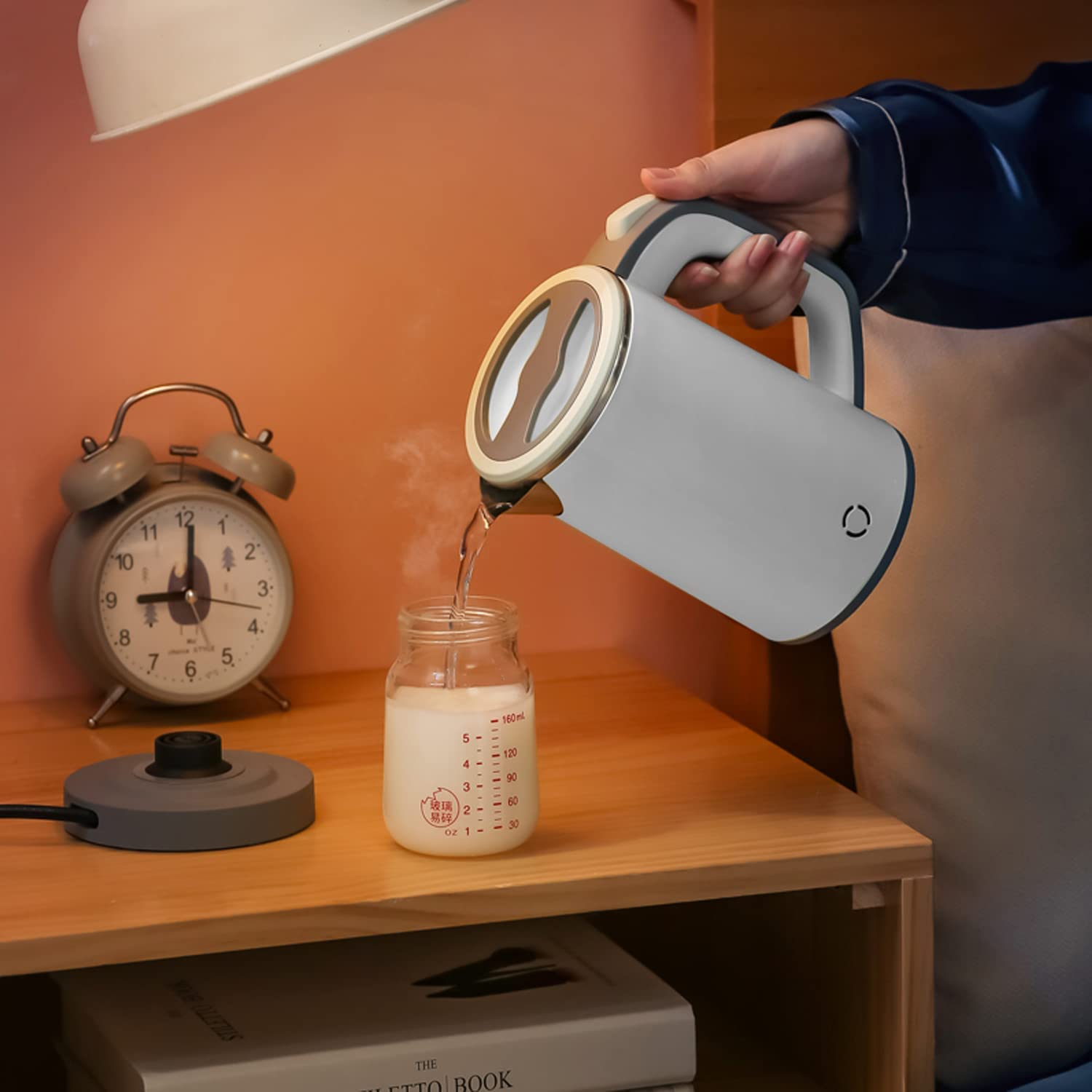 Eine Person gießt Wasser aus einem weiß-grauen Wasserkocher in eine Glasflasche auf einem Holztisch.