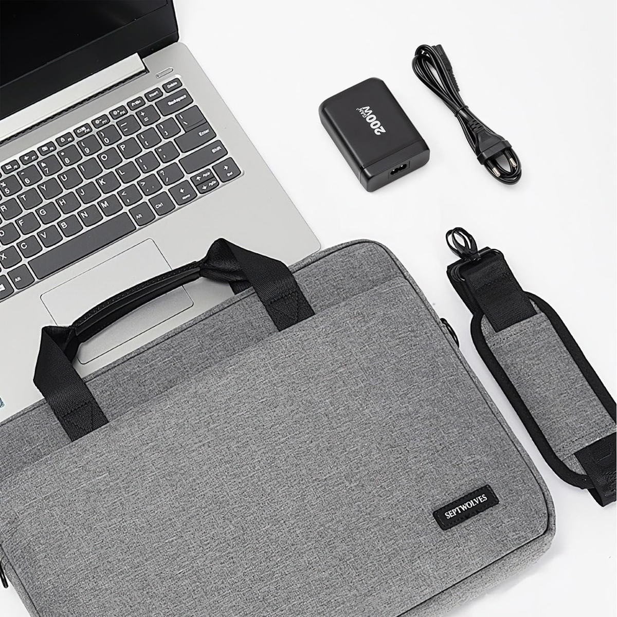 Laptop, Ladegerät, Tasche und Gurt auf weißer Oberfläche.