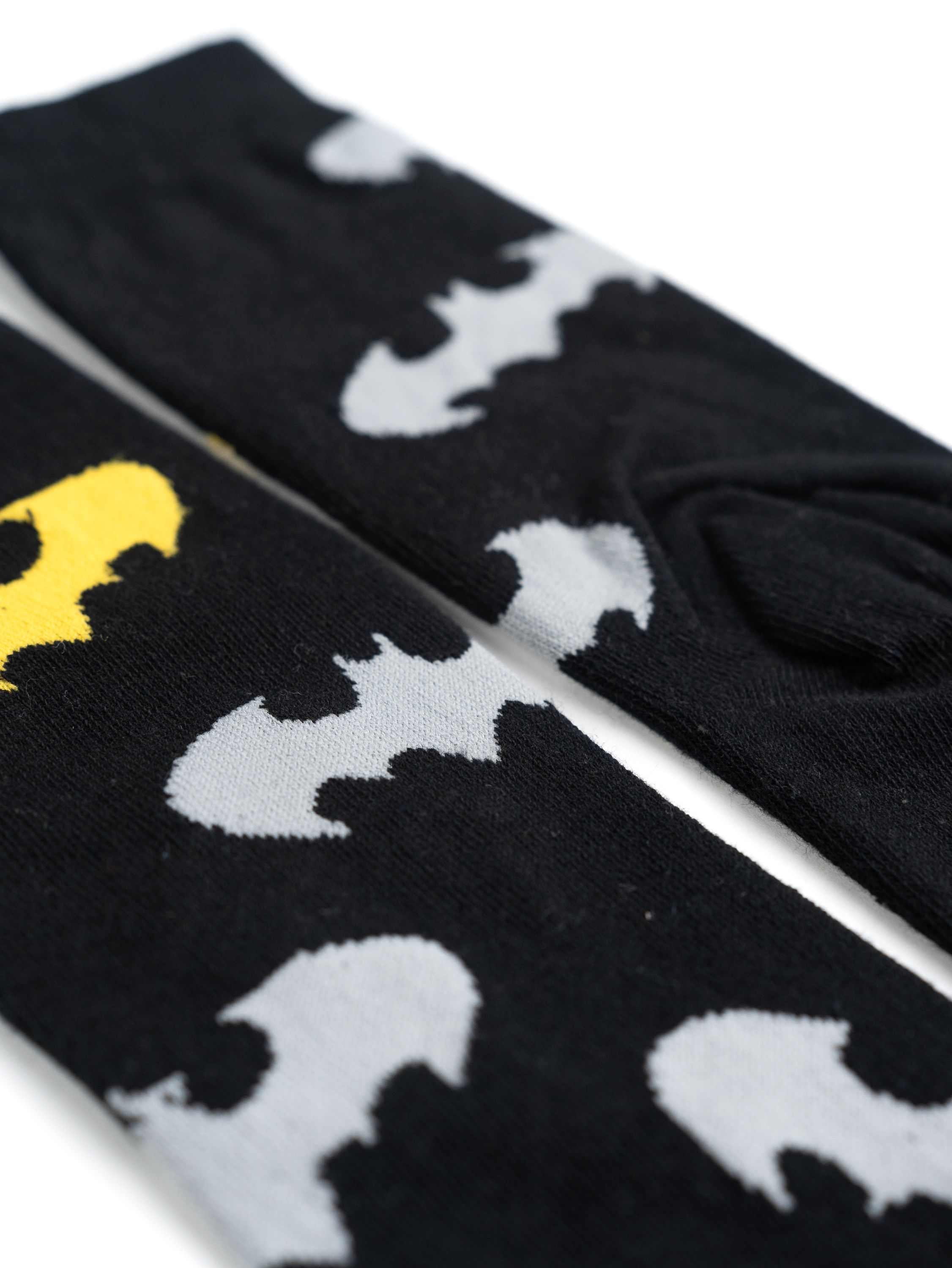 Zwei schwarze Socken mit grauen Batman-Symbolen. Die Socken sind auf weißem Hintergrund.