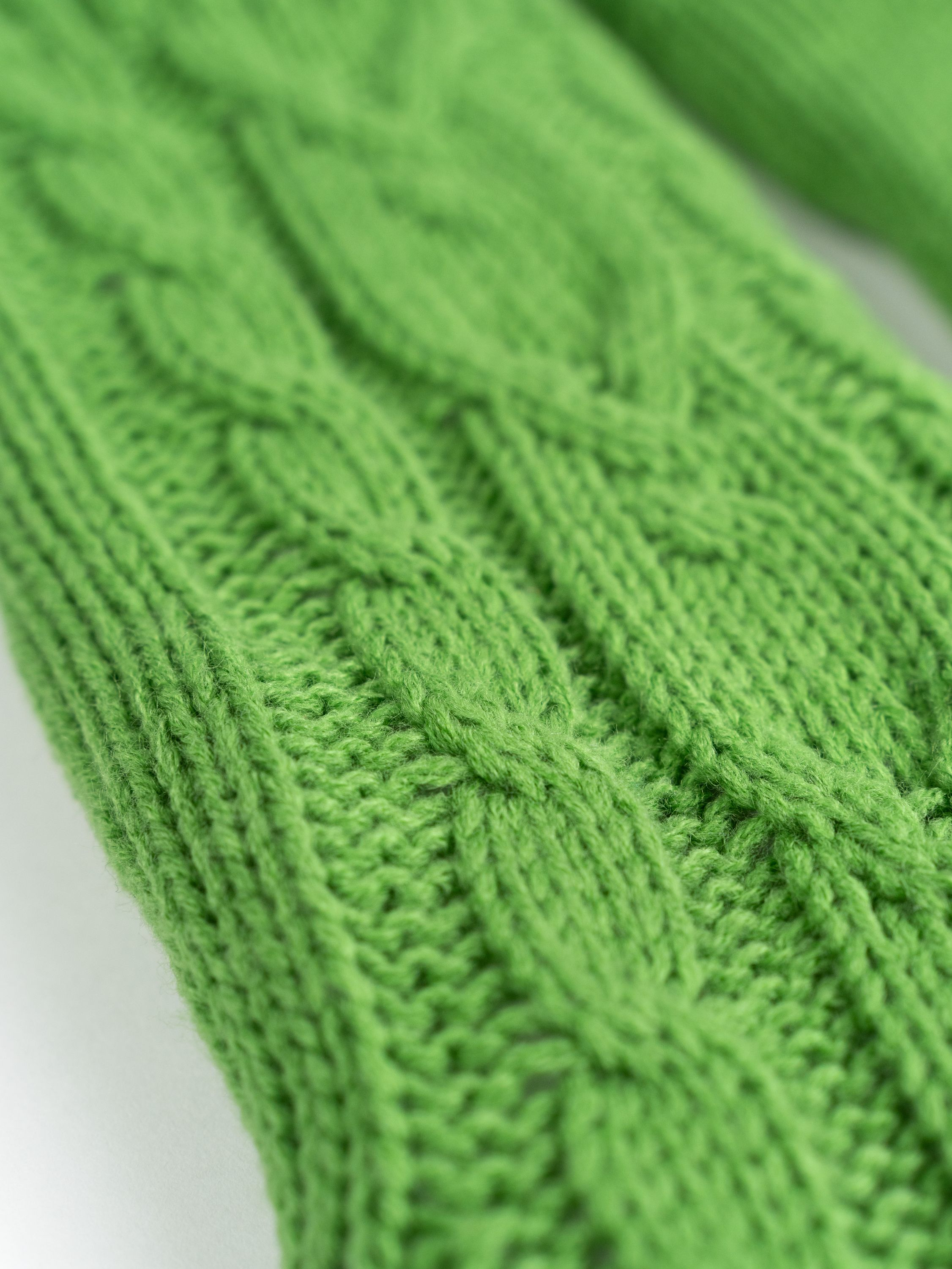 Nahaufnahme von grünem Strickstoff mit Zopfmuster.