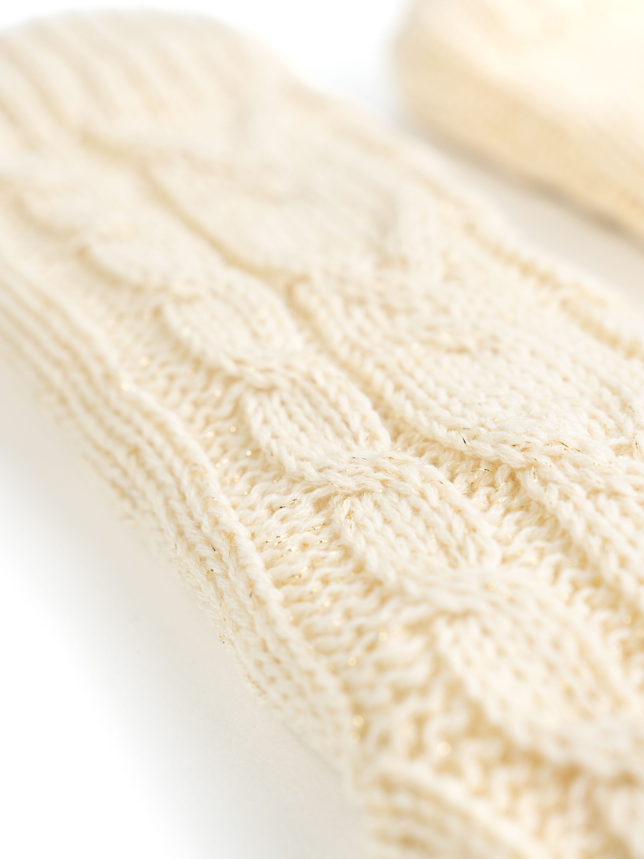Nahaufnahme von cremefarbenen gestrickten Beinlingen mit Goldfaden.