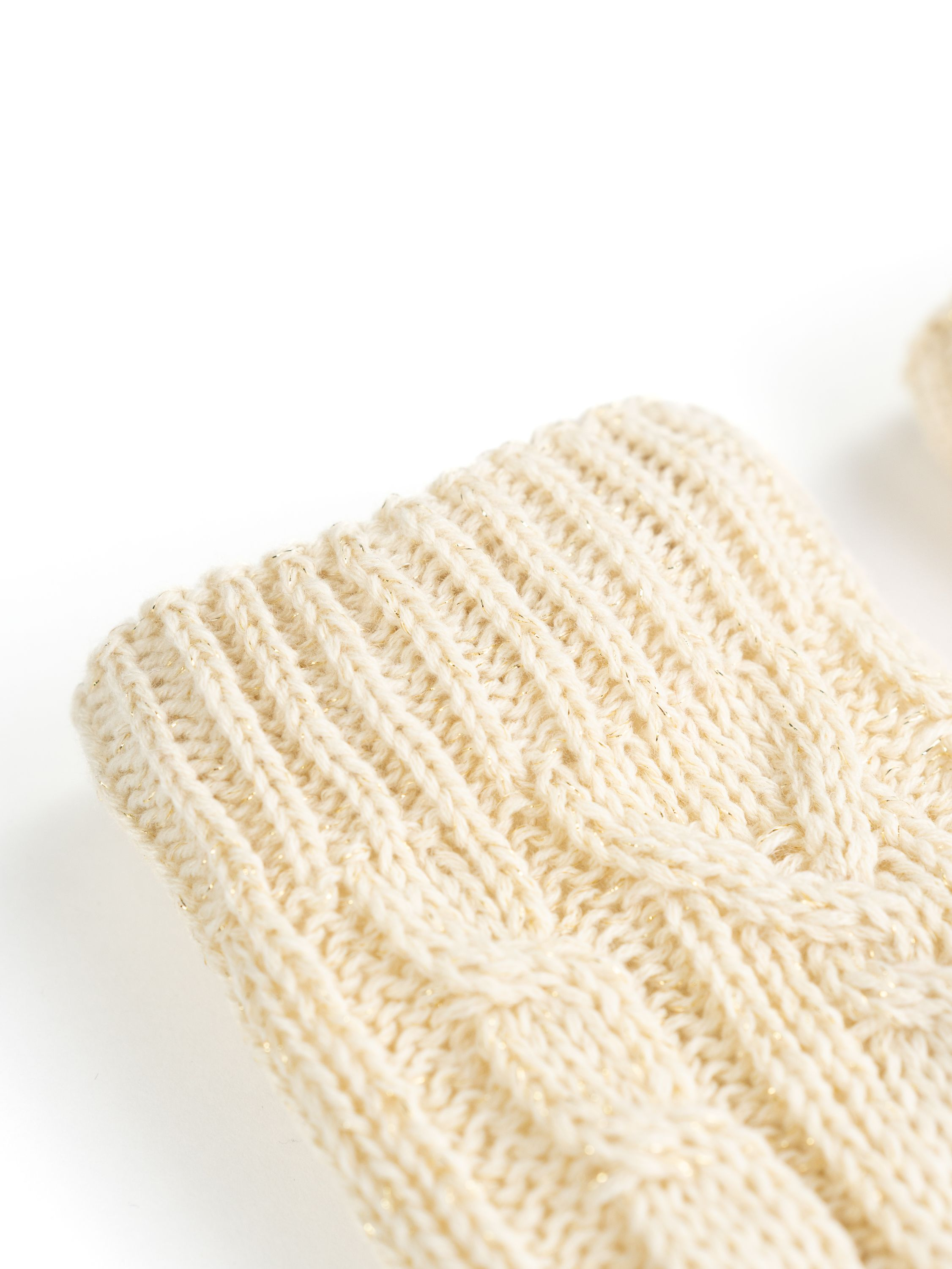 Nahaufnahme einer cremefarbenen Strickmanschette mit gemustertem Design und Goldfäden.