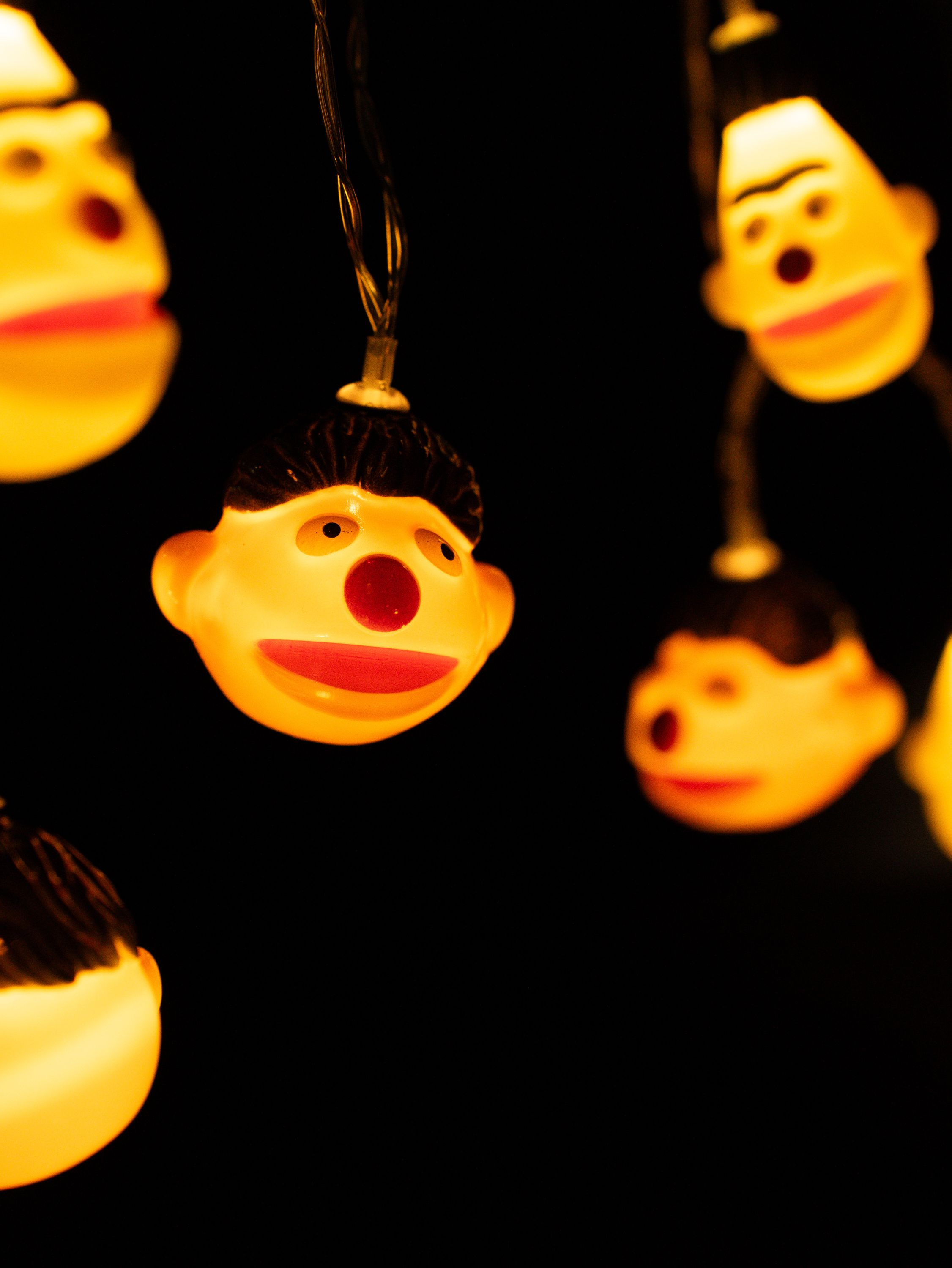 Nahaufnahme von Lichterketten mit Cartoon-Gesichtsschmuck; gelb beleuchtet vor schwarzem Hintergrund.