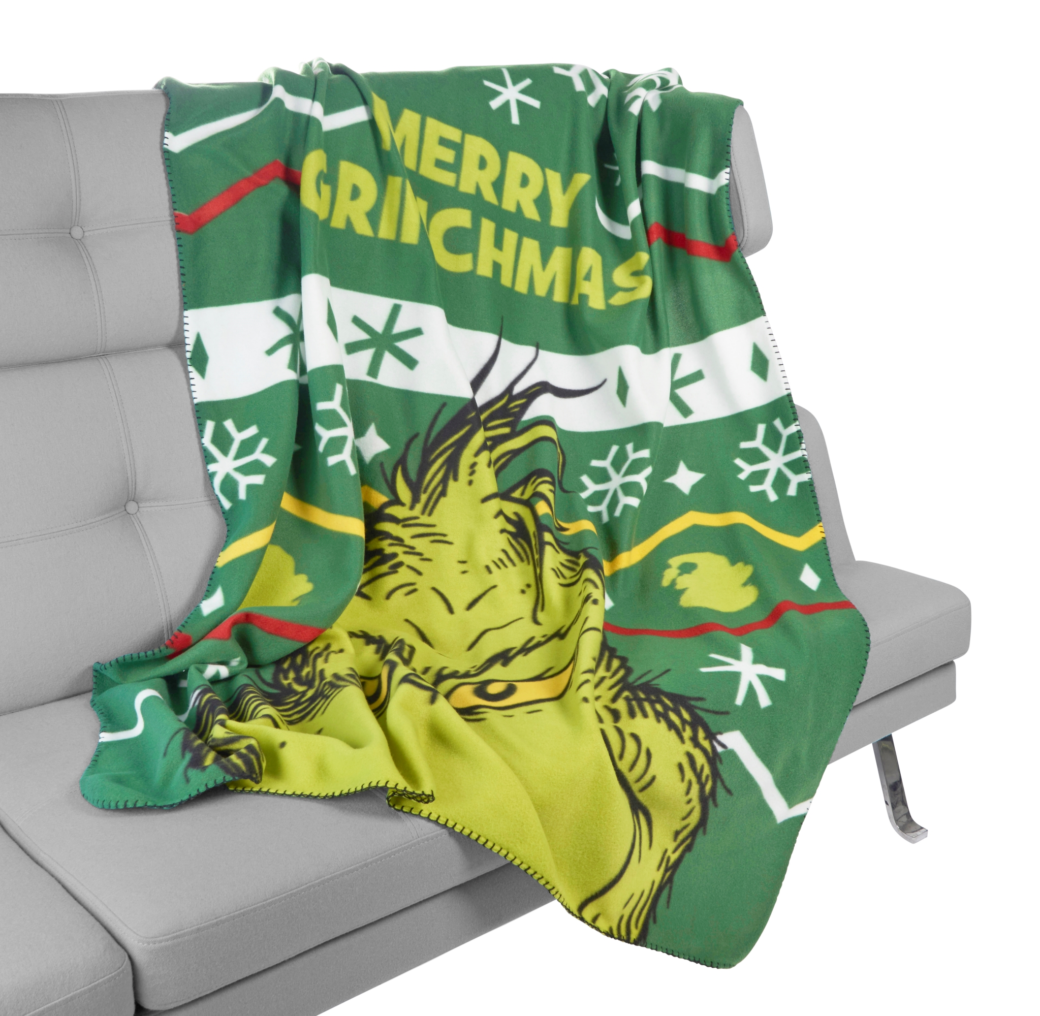 Eine grüne Decke mit einem Grinch-Bild und dem Text 'Merry Grinchmas' auf einer grauen Couch.