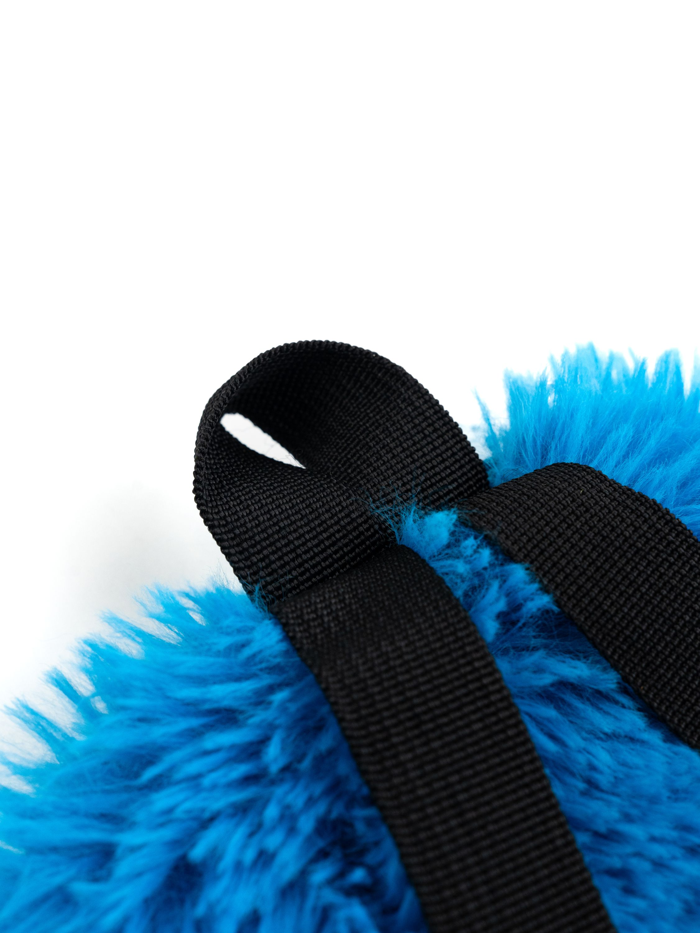 Nahaufnahme eines flauschigen, blauen, pelzigen Materials mit schwarzem Riemen auf weißem Hintergrund.