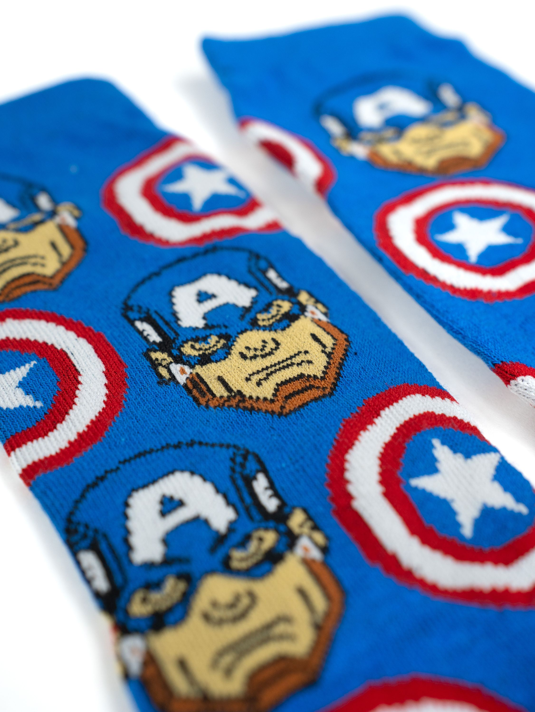 Nahaufnahme von zwei blauen Socken mit Captain America-Design. Die Socken liegen auf einer weißen Oberfläche.